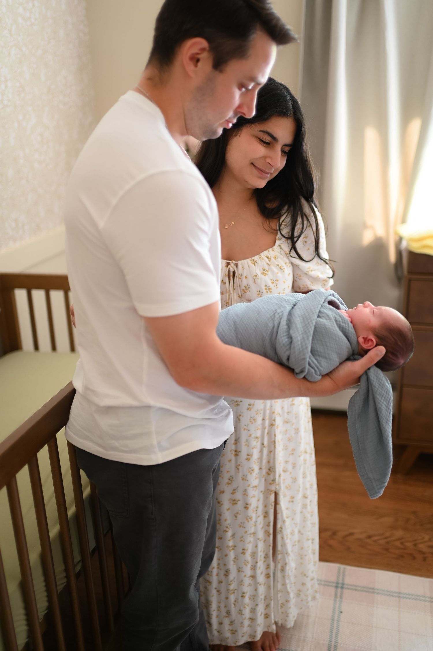 Parents tenderly hold their newborn baby in a nursery setting with natural lighting.