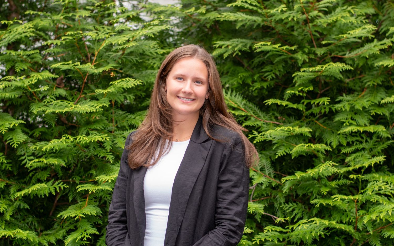 Professional headshot in front of lush green cypress trees.