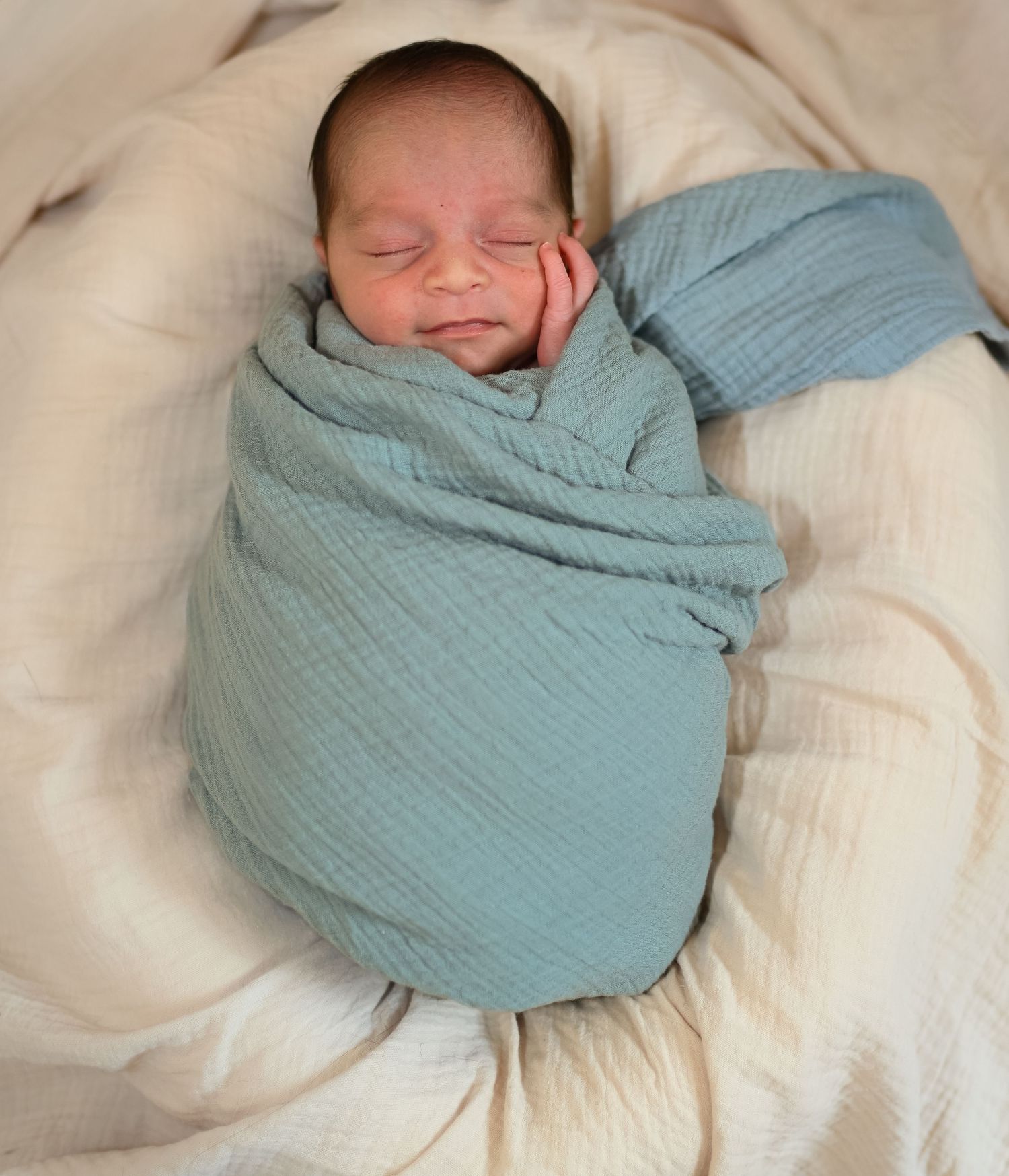 Sleeping newborn wrapped in soft mint green swaddle on cream bedding.
