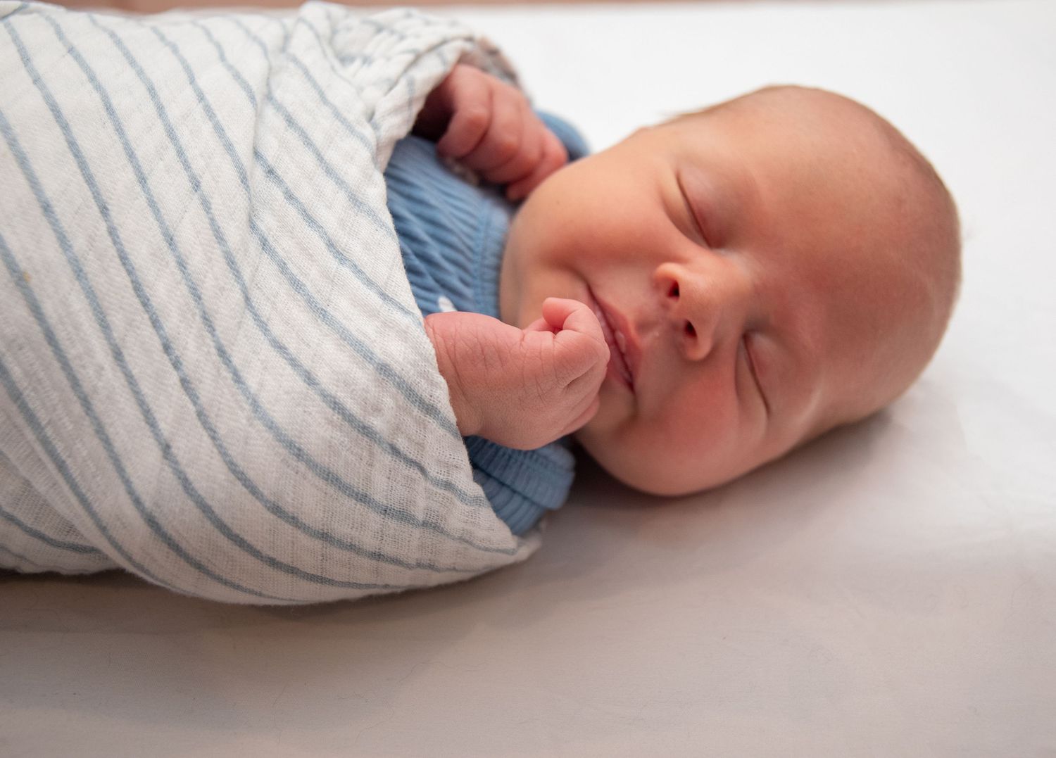 Baby wrapped in striped swaddle blanket shown in series of peaceful sleeping poses.