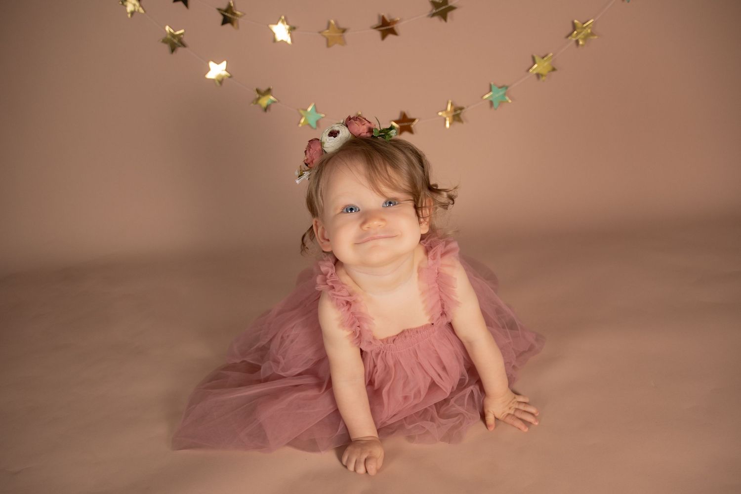 Pink backdrop with hanging gold stars creates dreamy setting for baby photography.