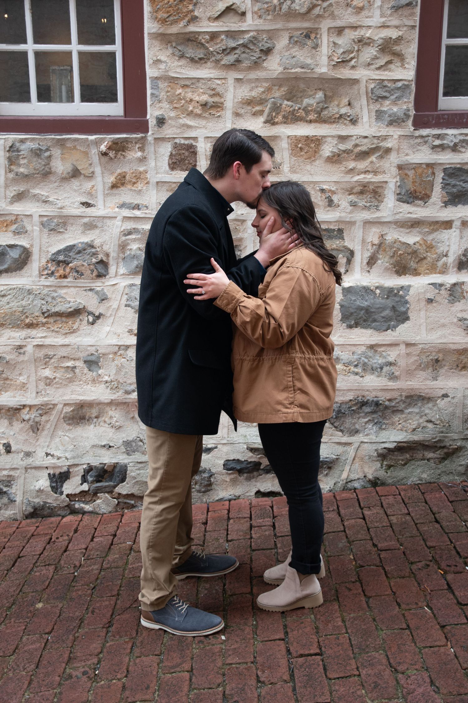 Sweet moment shared between couple on brick pathway by stone building.