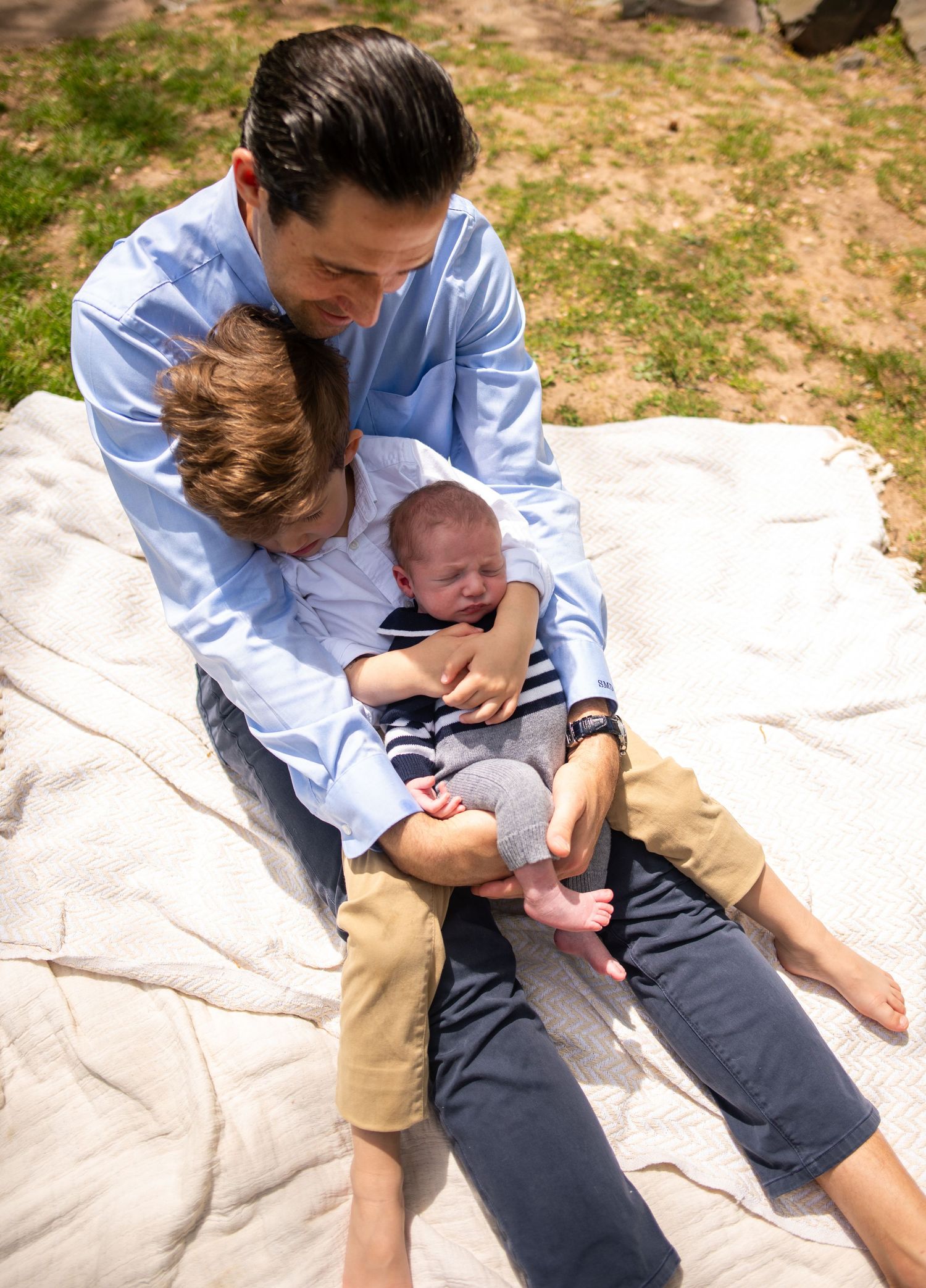 Family enjoying outdoor time together on white blanket in sunlit park.