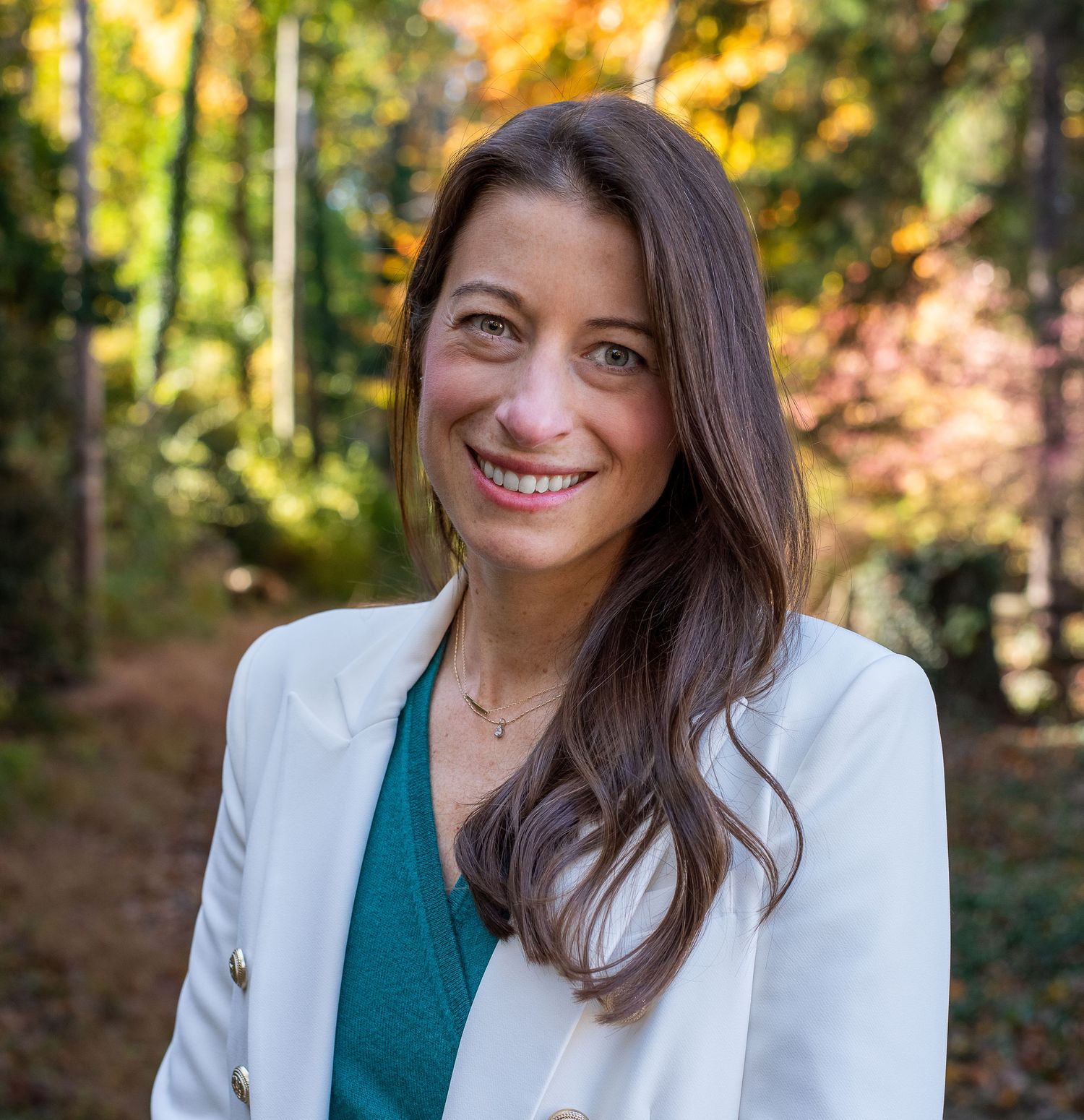 Outdoor portrait series wearing a white blazer and green top with autumn foliage in background.