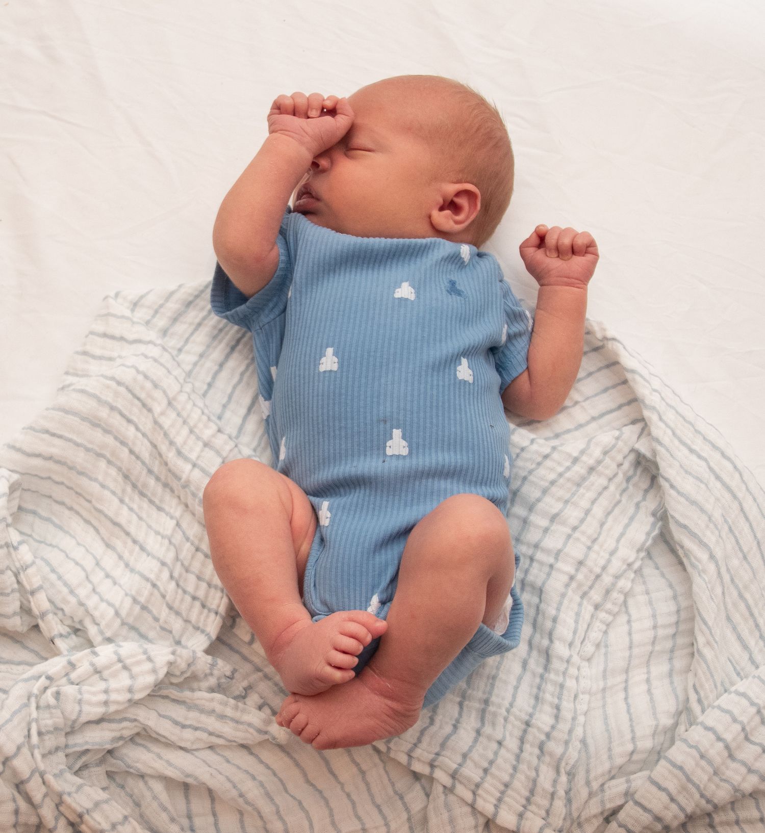 Baby wearing blue onesie resting on striped blanket in various poses.