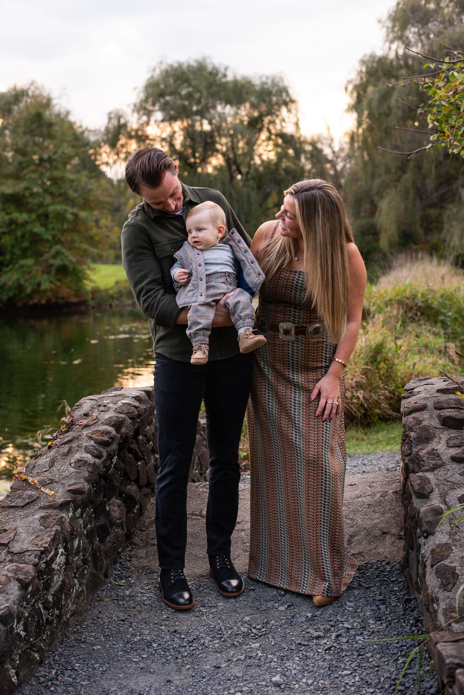 A family shares tender moments along a stone path during an outdoor autumn photo session at sunset.