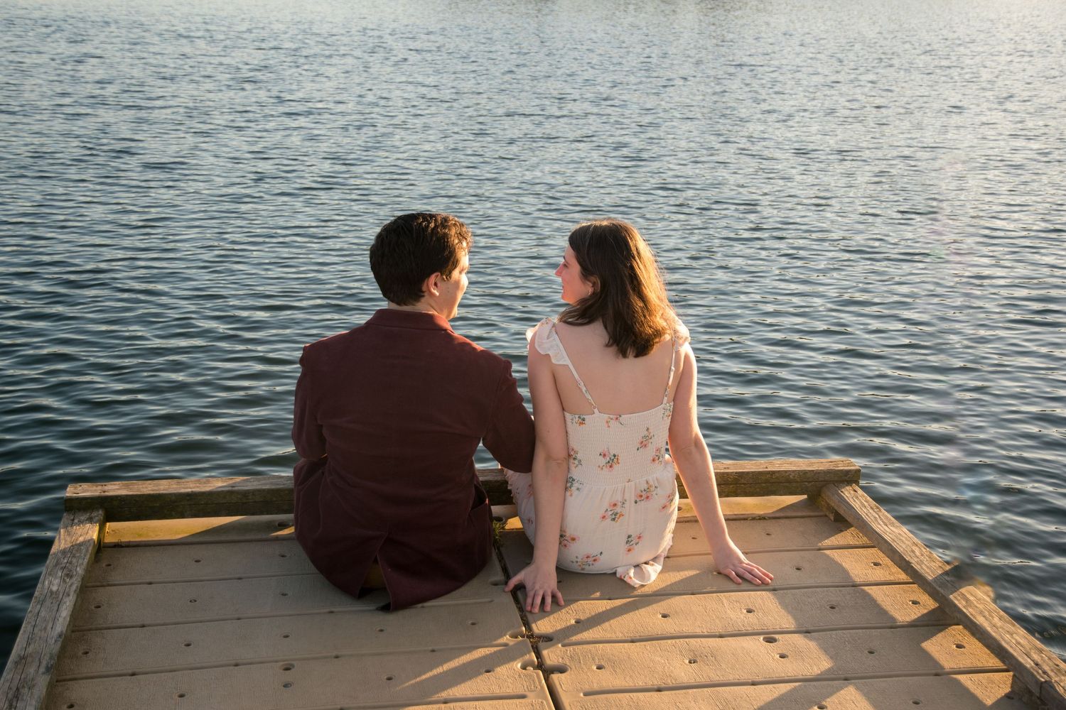 Couple sits together on a wooden dock by a serene lake during golden hour.
