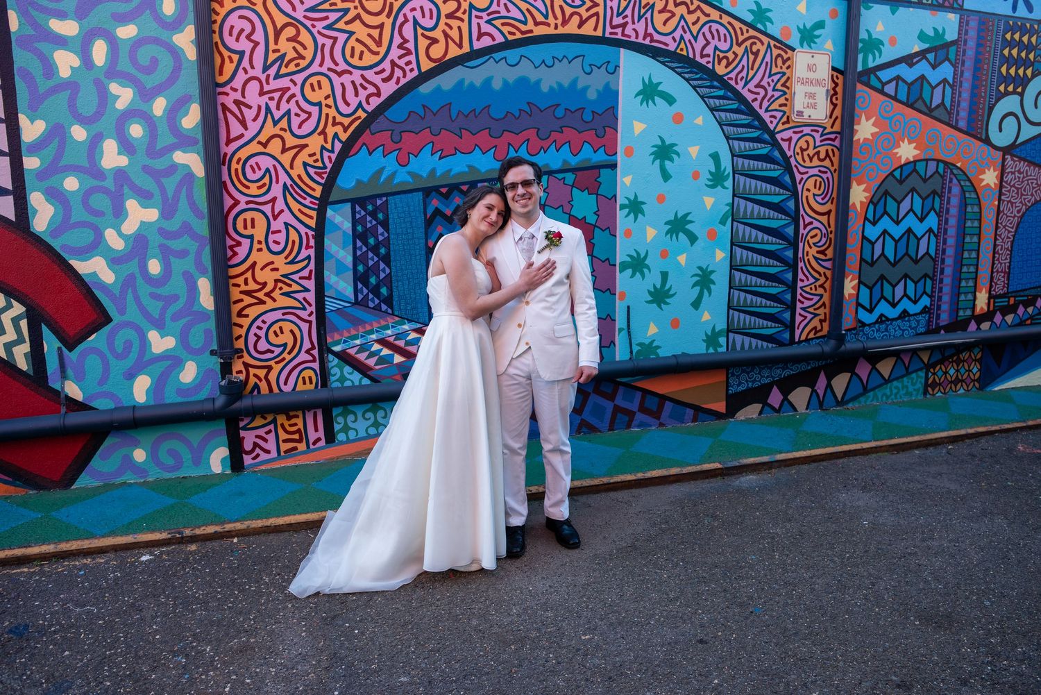A wedding couple poses in front of a vibrant blue and pink graffiti mural.