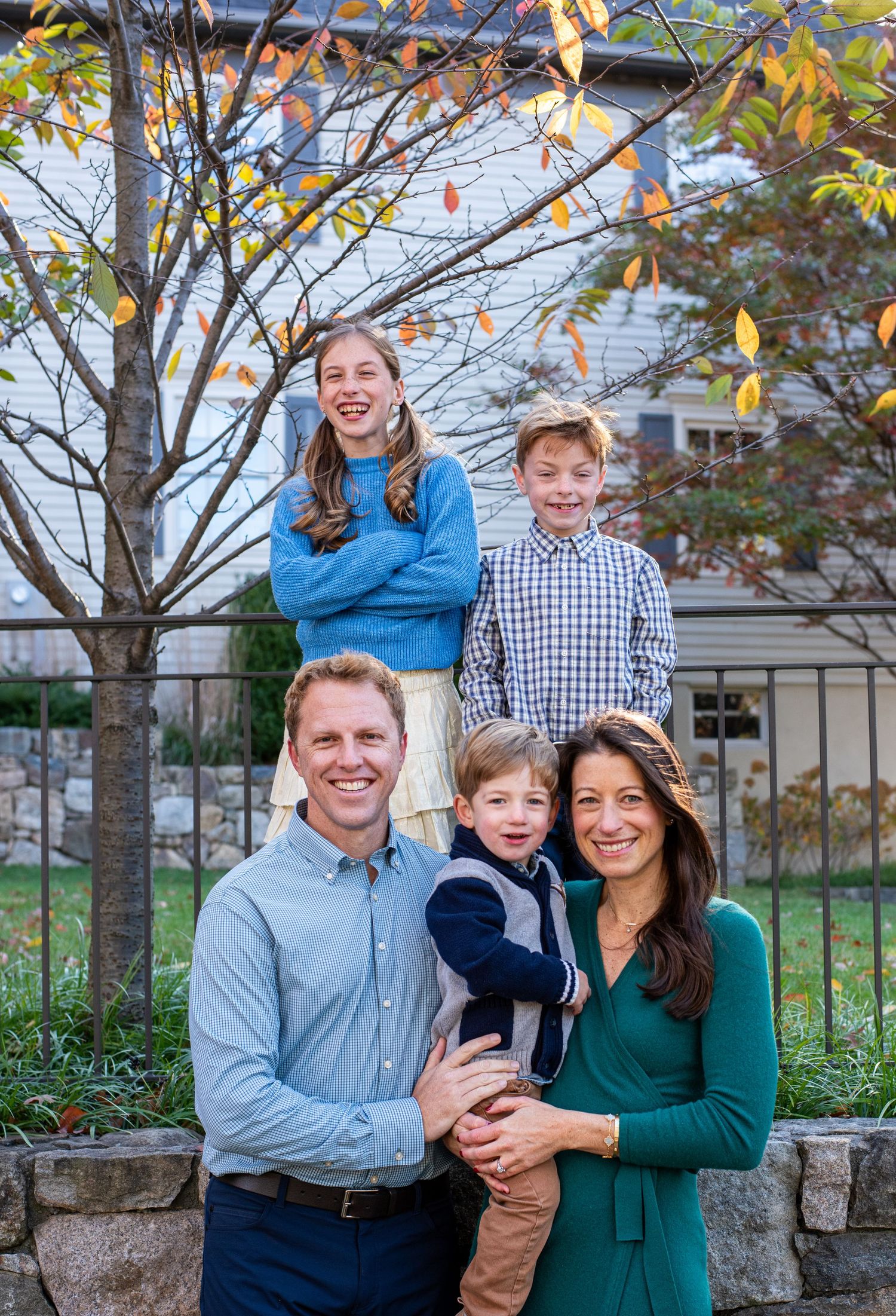A family photo session outdoors with trees and autumn colors in the background.