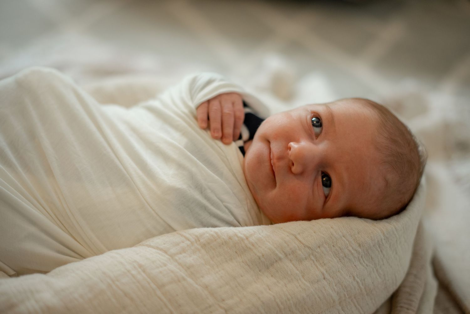 Close-up of an alert newborn baby wrapped in white swaddling.