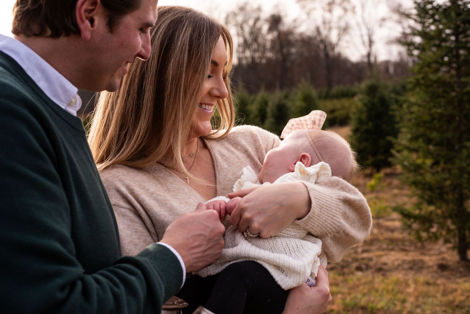 Tender family moment outdoors with evergreen trees in background at sunset.