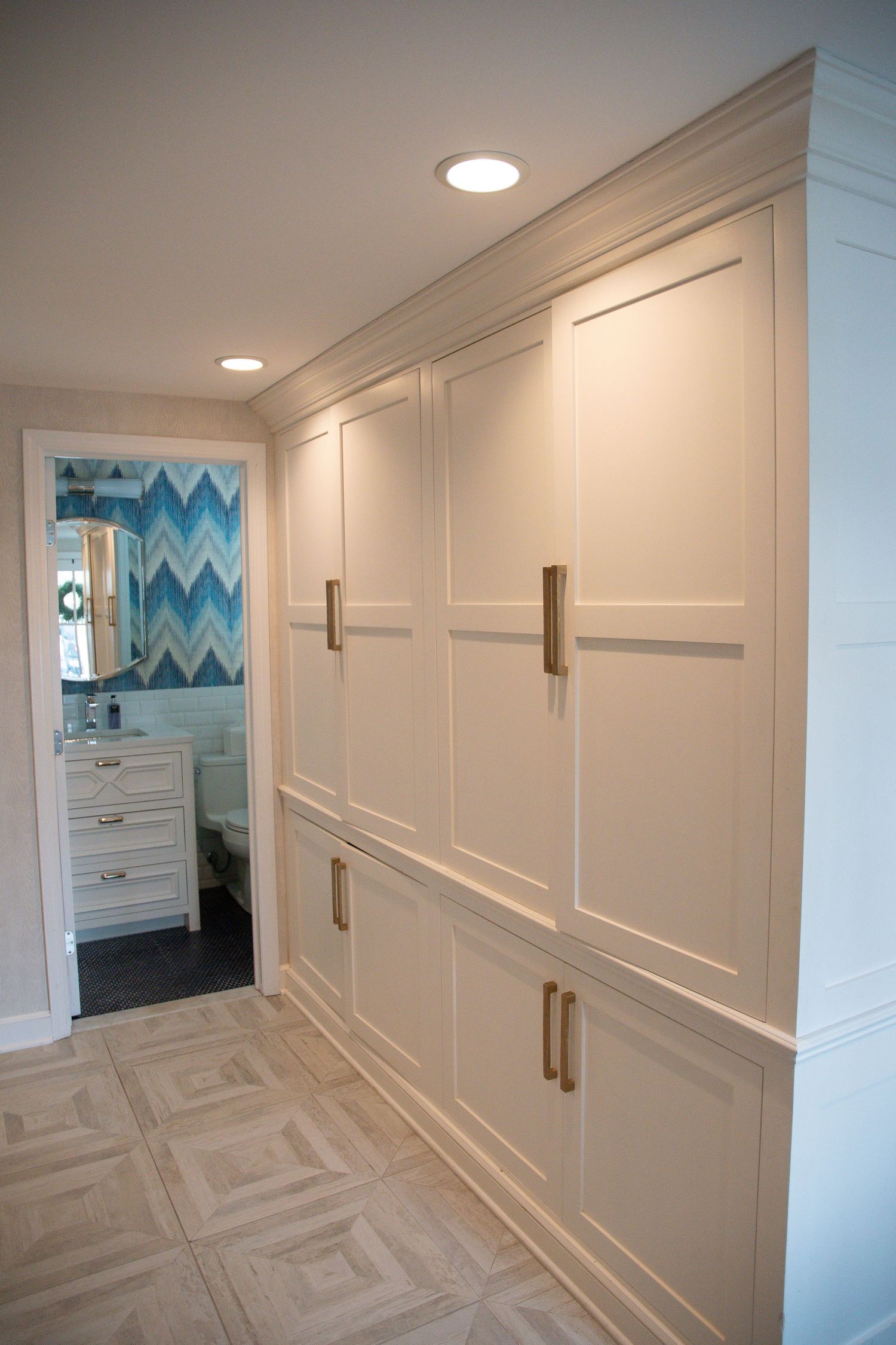 Hallway with white paneled walls, molding details, and herringbone pattern flooring.