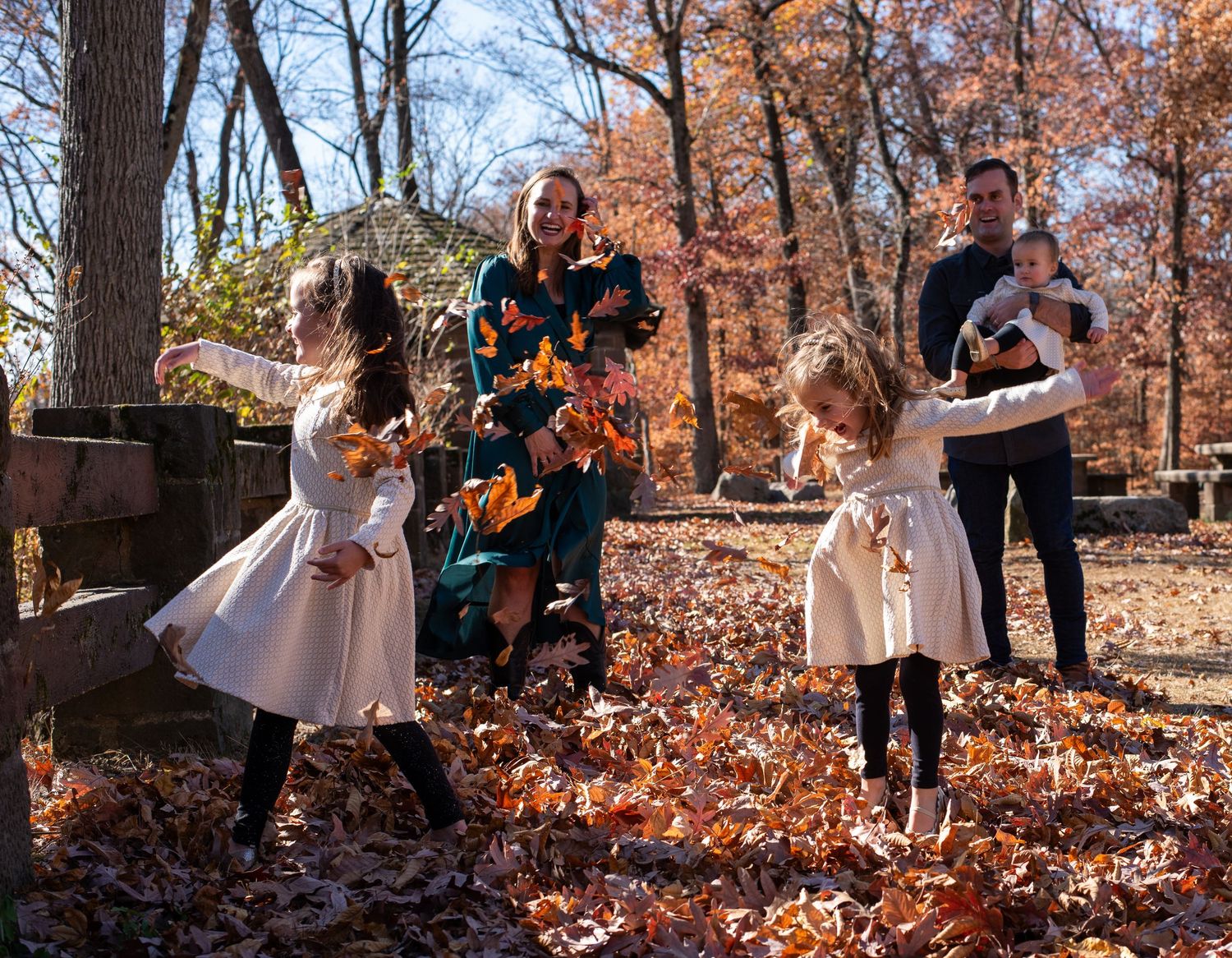 A joyful outdoor family photoshoot with fallen autumn leaves in a wooded setting.