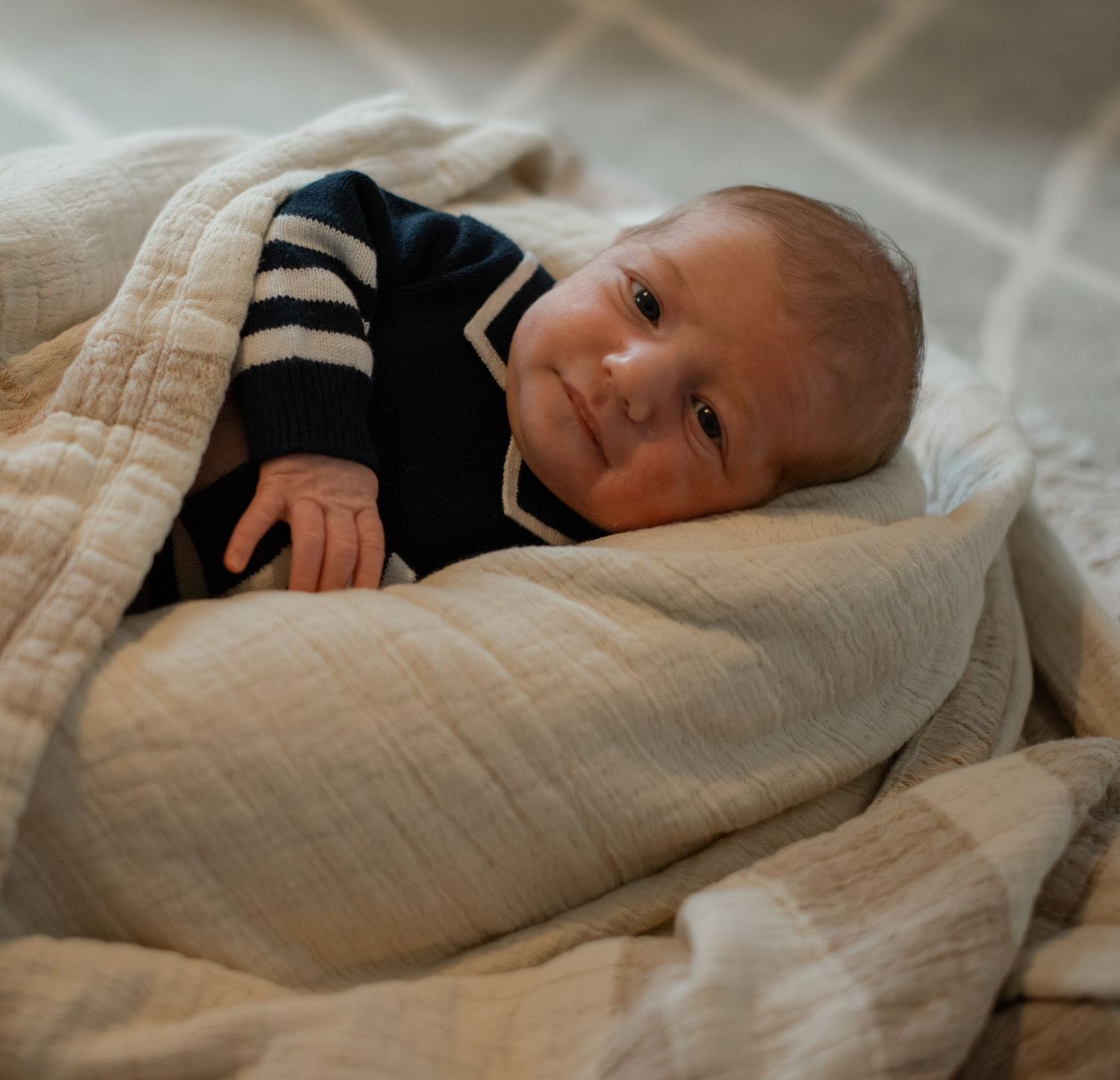 Baby in neutral colored swaddle lying on soft textured bedding.