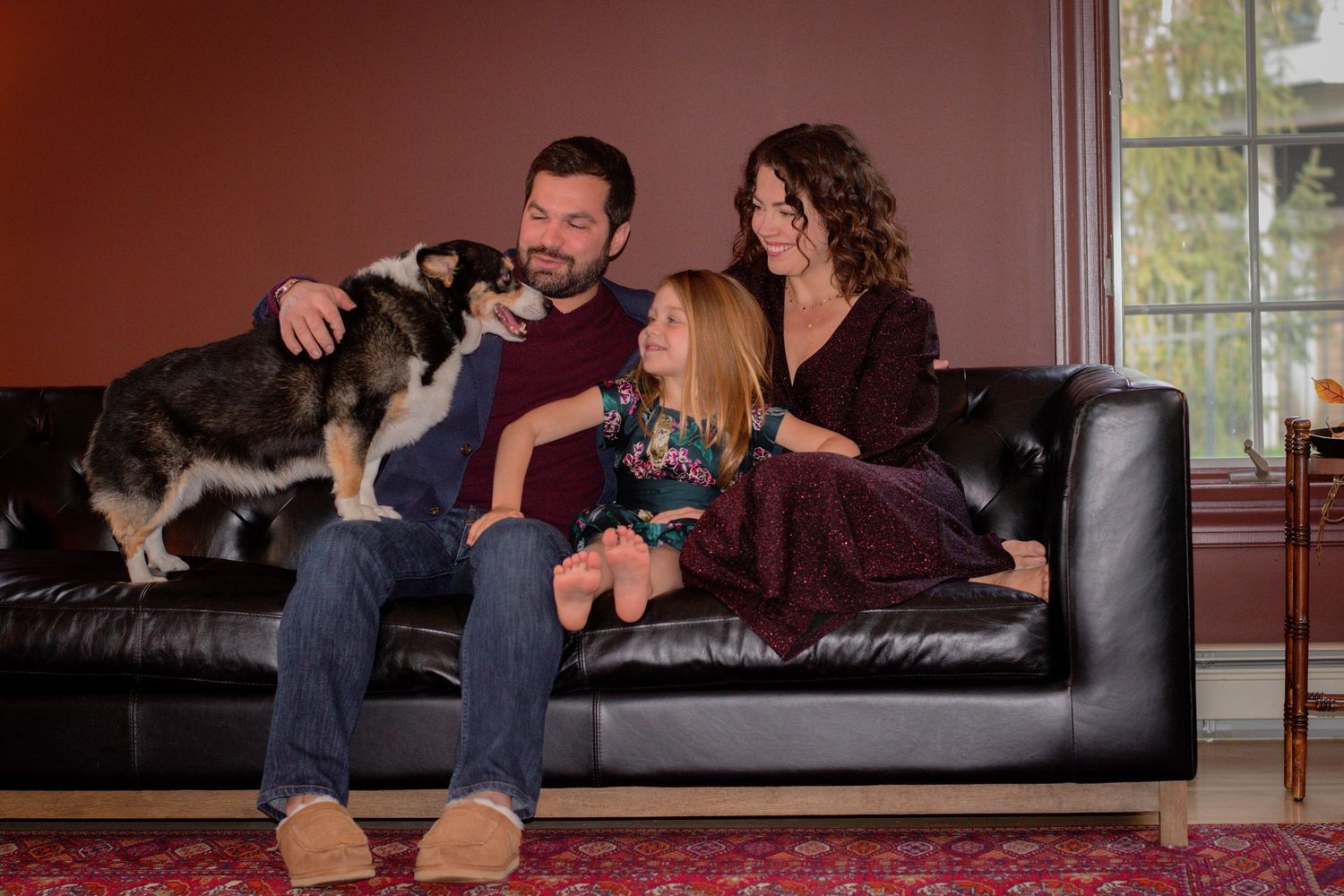 A casual family photo session on a dark leather couch indoors.