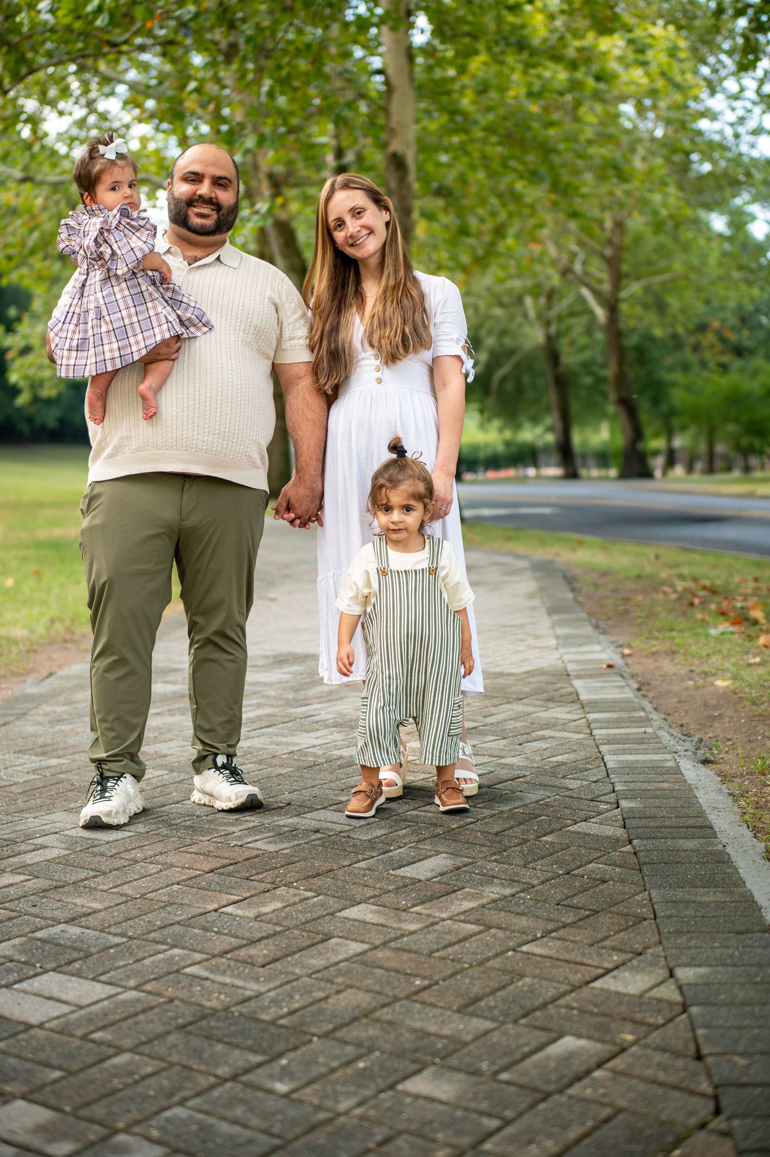 A family enjoys a walk together on a brick pathway in a green park on a sunny day.
