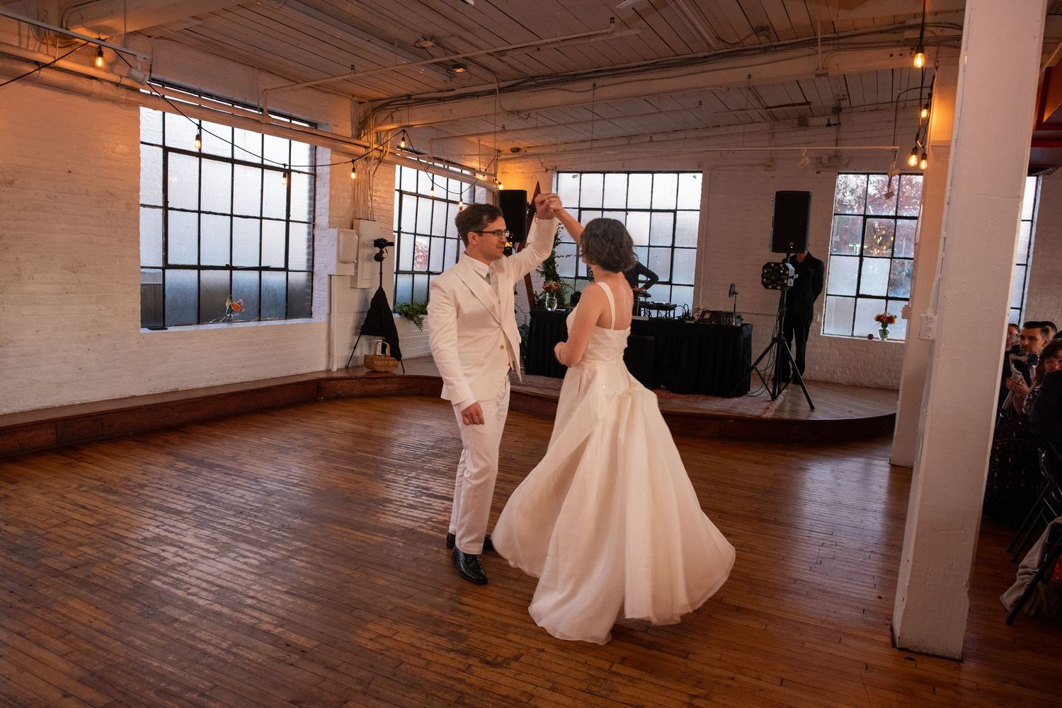A couple shares their first dance in an industrial loft space with large windows.