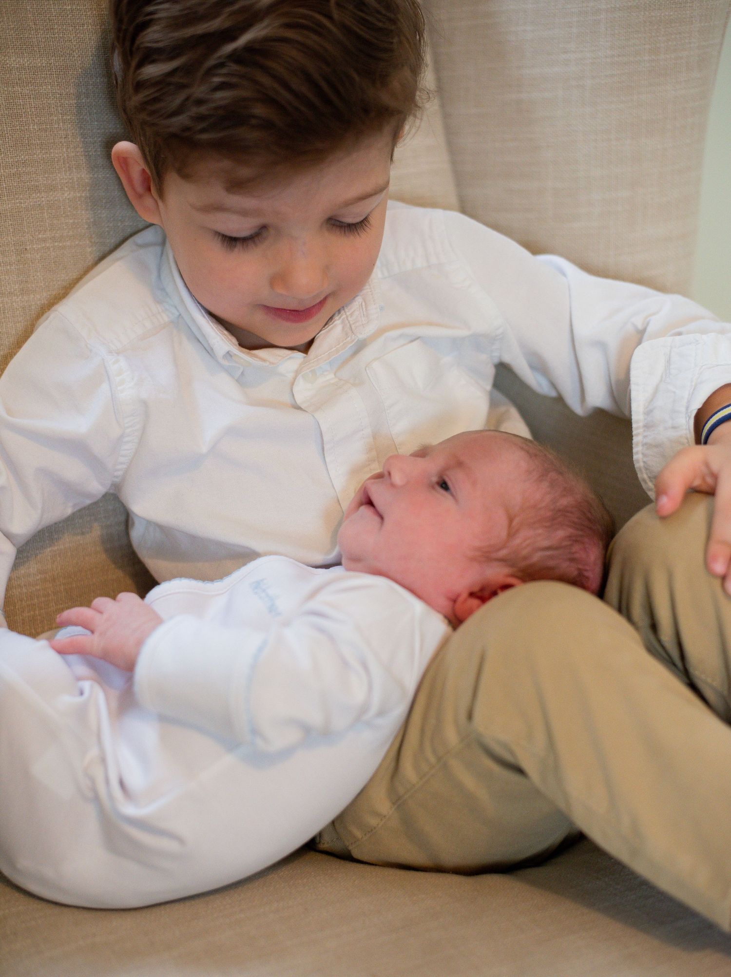 Children in white shirts share tender moment on beige furniture.