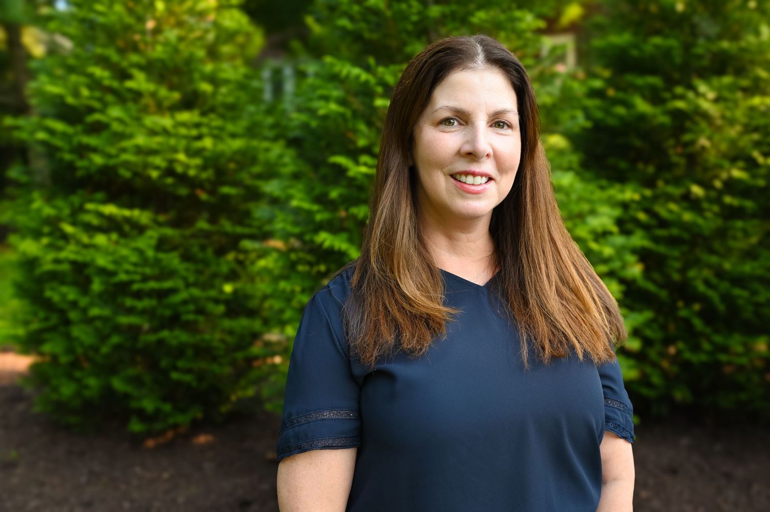 Professional headshots against a natural green foliage background wearing a navy top.