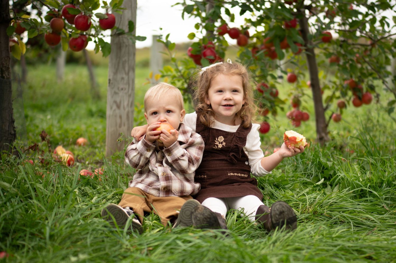 A child sits in green grass surrounded by falling autumn leaves in a whimsical outdoor portrait session.