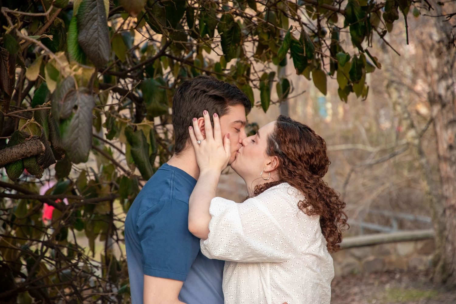 Romantic couple embraces under leafy tree branches during outdoor photoshoot.