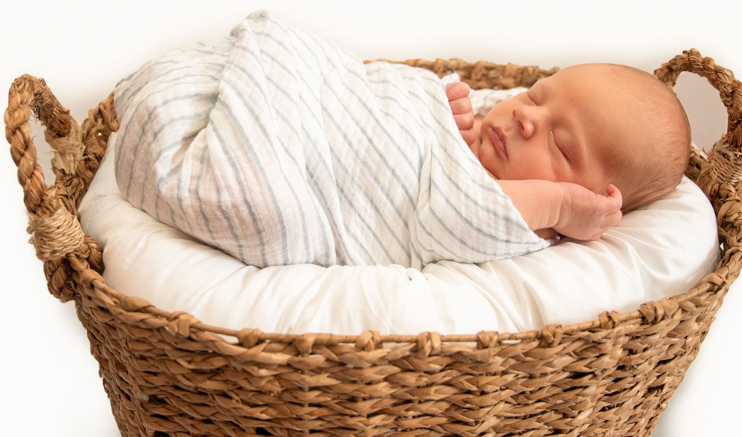 Sleeping newborn wrapped in white blanket lying in woven basket.