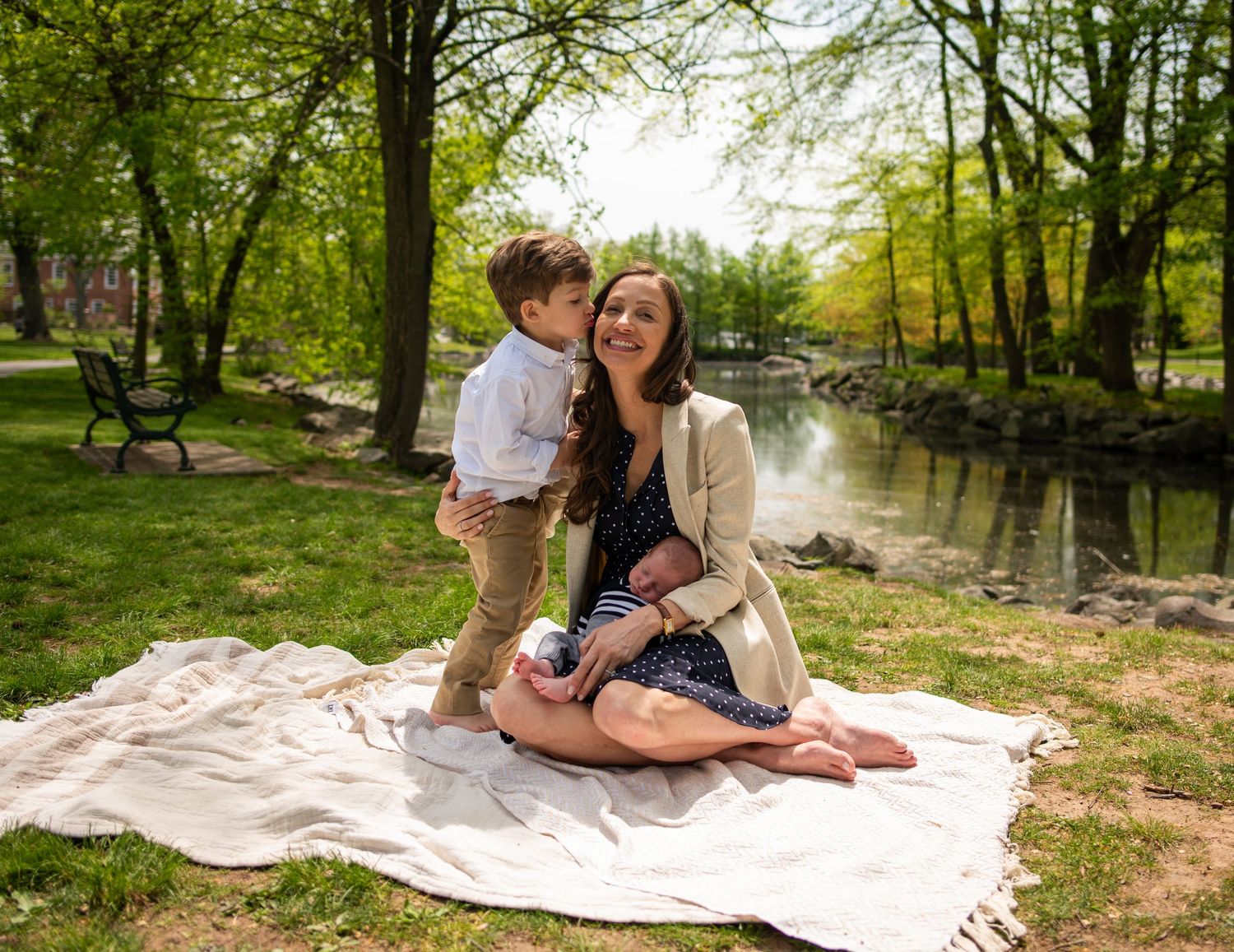 Family enjoying a sunny day on picnic blanket by pond in park setting.