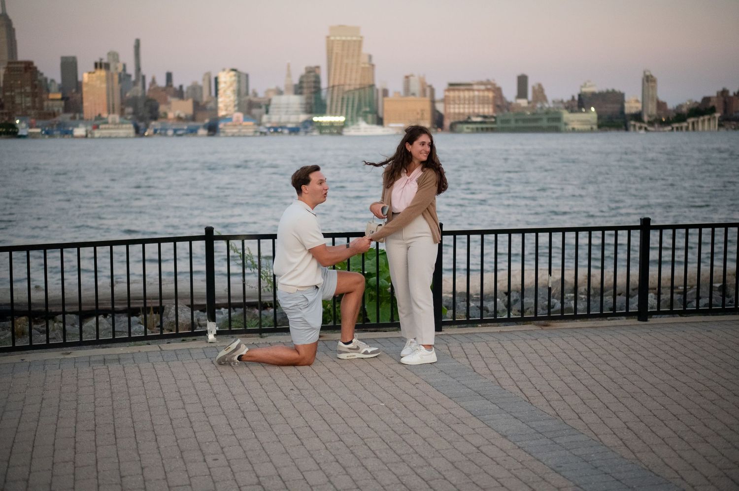 Young couples enjoying summer evening by waterfront pier with city skyline and Hudson River in background.