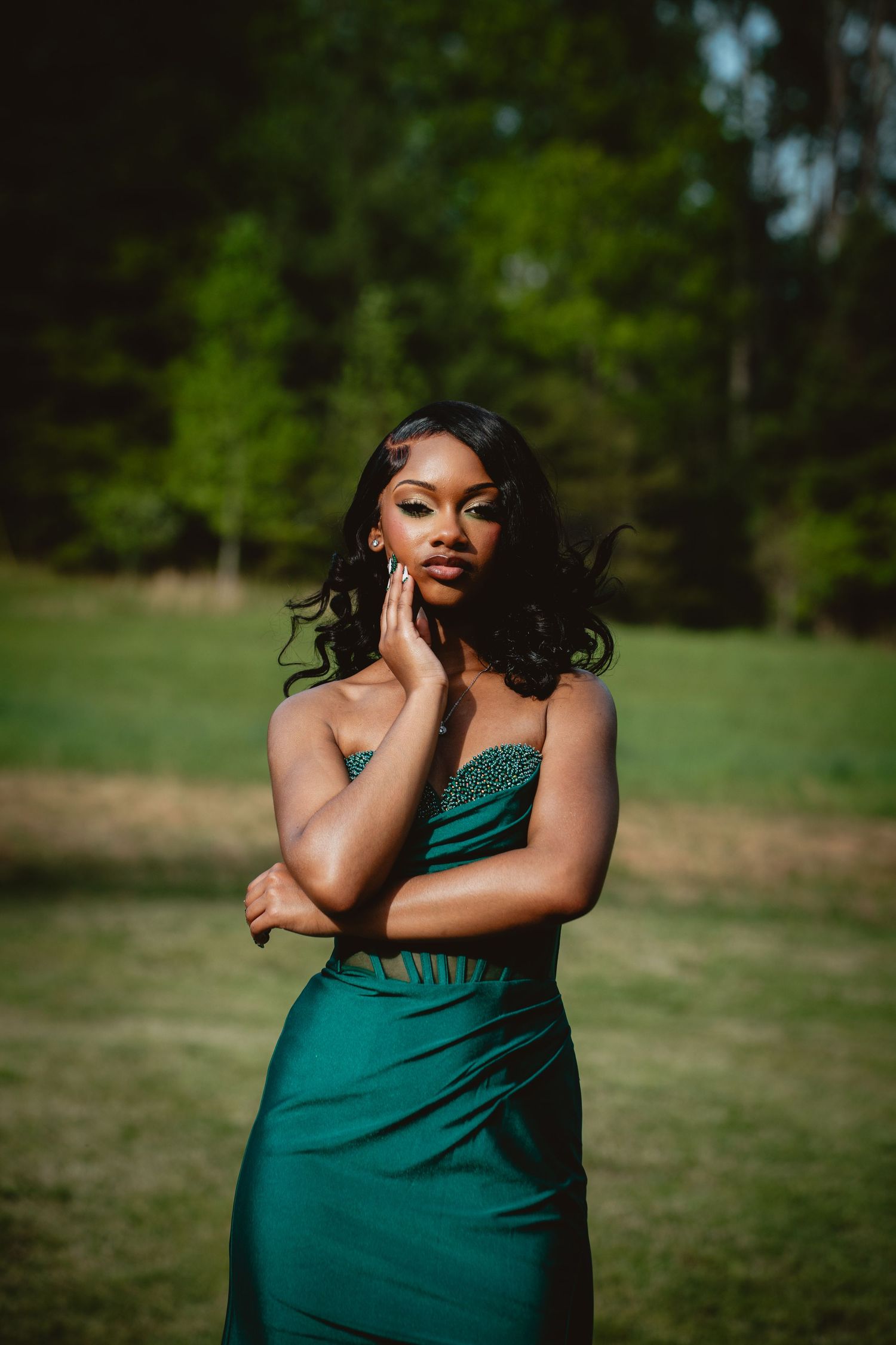 A person wearing a green dress poses gracefully in an outdoor photoshoot with natural lighting and lush greenery.