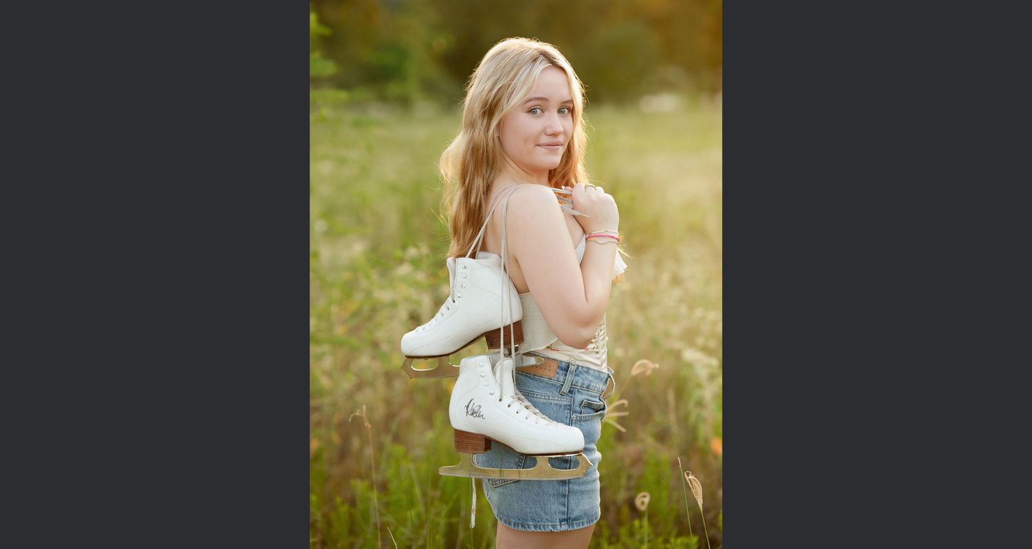 ice skater senior photos in a field.  ice skates over the shoulder senior photos.  the woodlands senior photographsr.