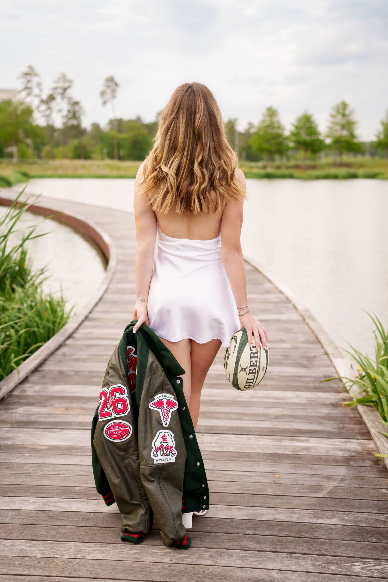 Rugby girl walking away with ball and letterman jacket.  woodlands rugby player senior photos.