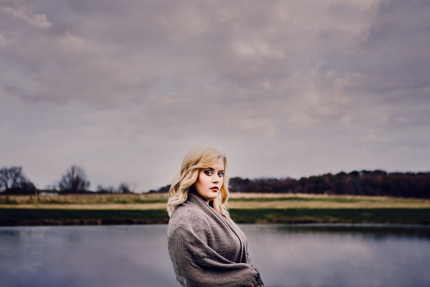 Fine art portrait of a woman wrapped in gray, standing by a misty lake — calm, cinematic, and moody light captured by ja’nicole;art