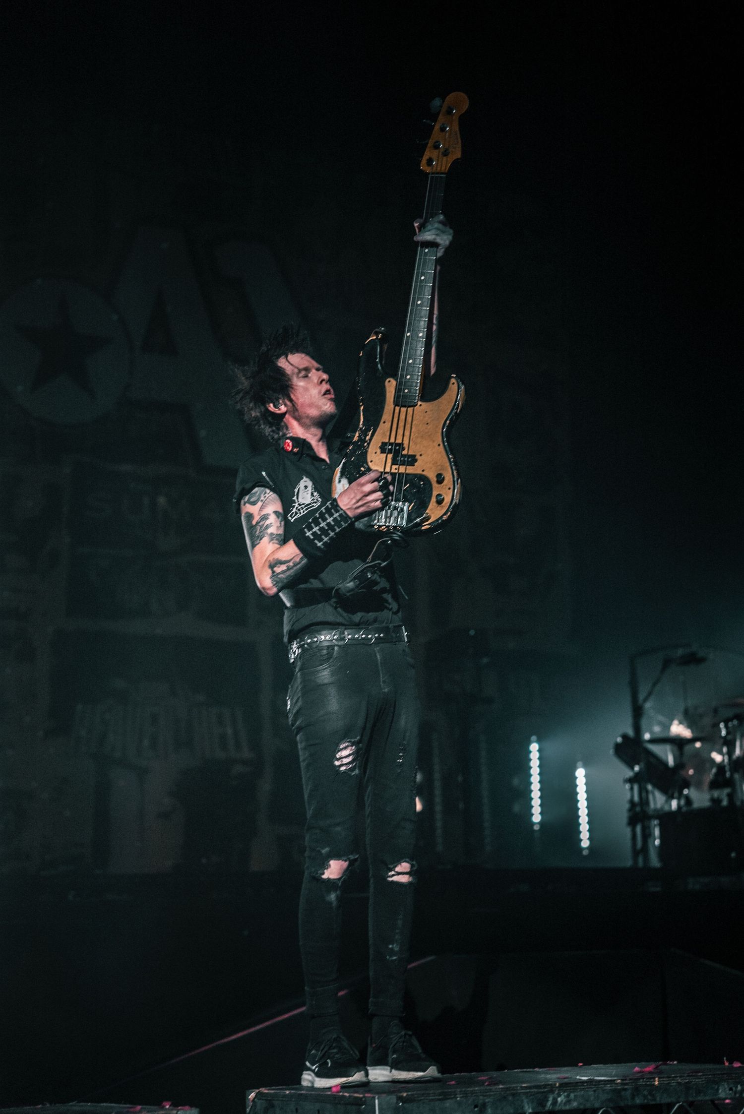 Musician plays bass guitar on dark stage with moody lighting effects.