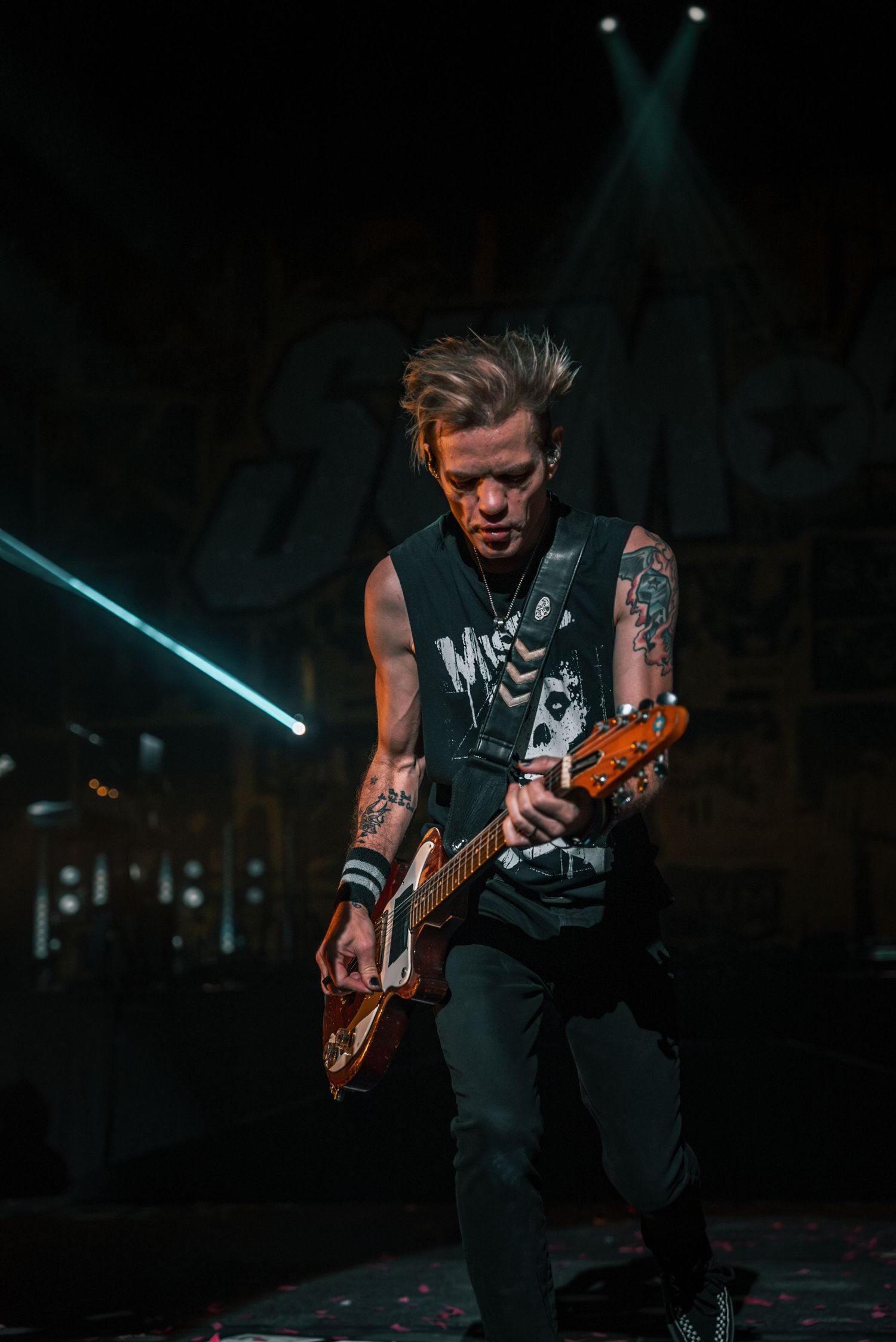 Tattooed musician plays guitar intensely during dark concert performance.