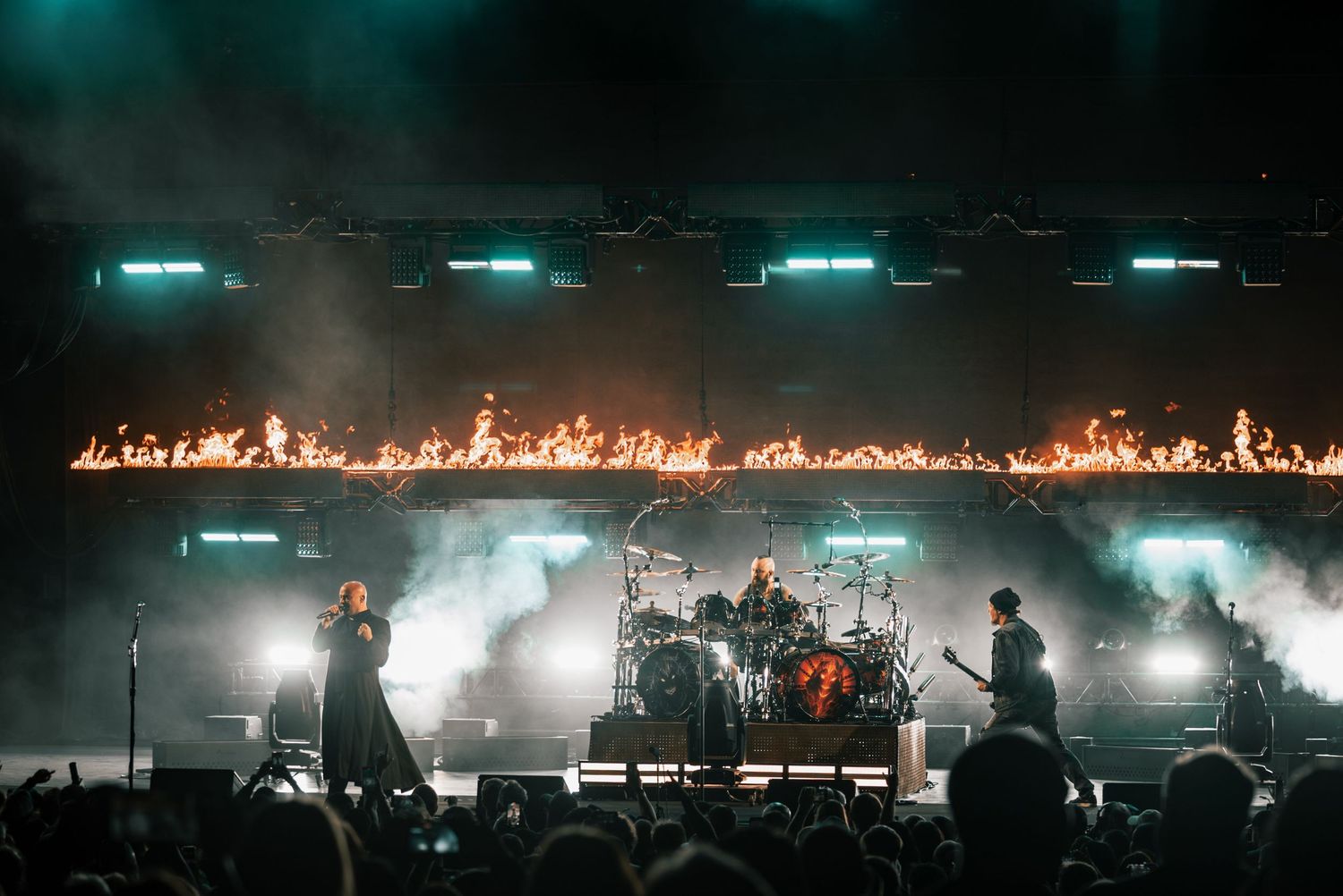 Band performs on stage with dramatic fire effects and fog creating an epic atmosphere.