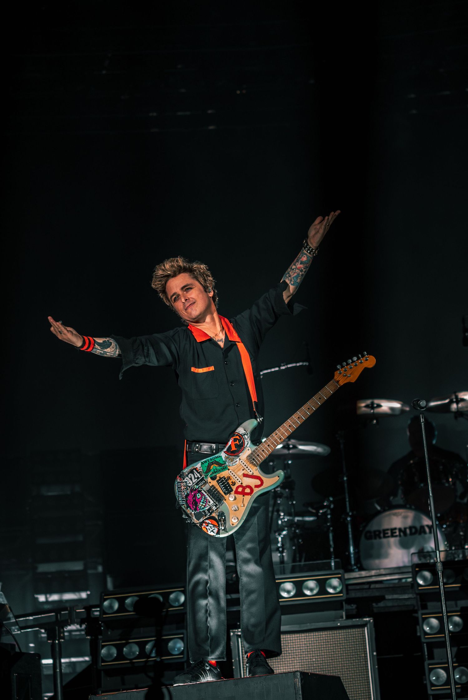 Dynamic wide-angle concert shot showing guitarist performing on dark stage with equipment.