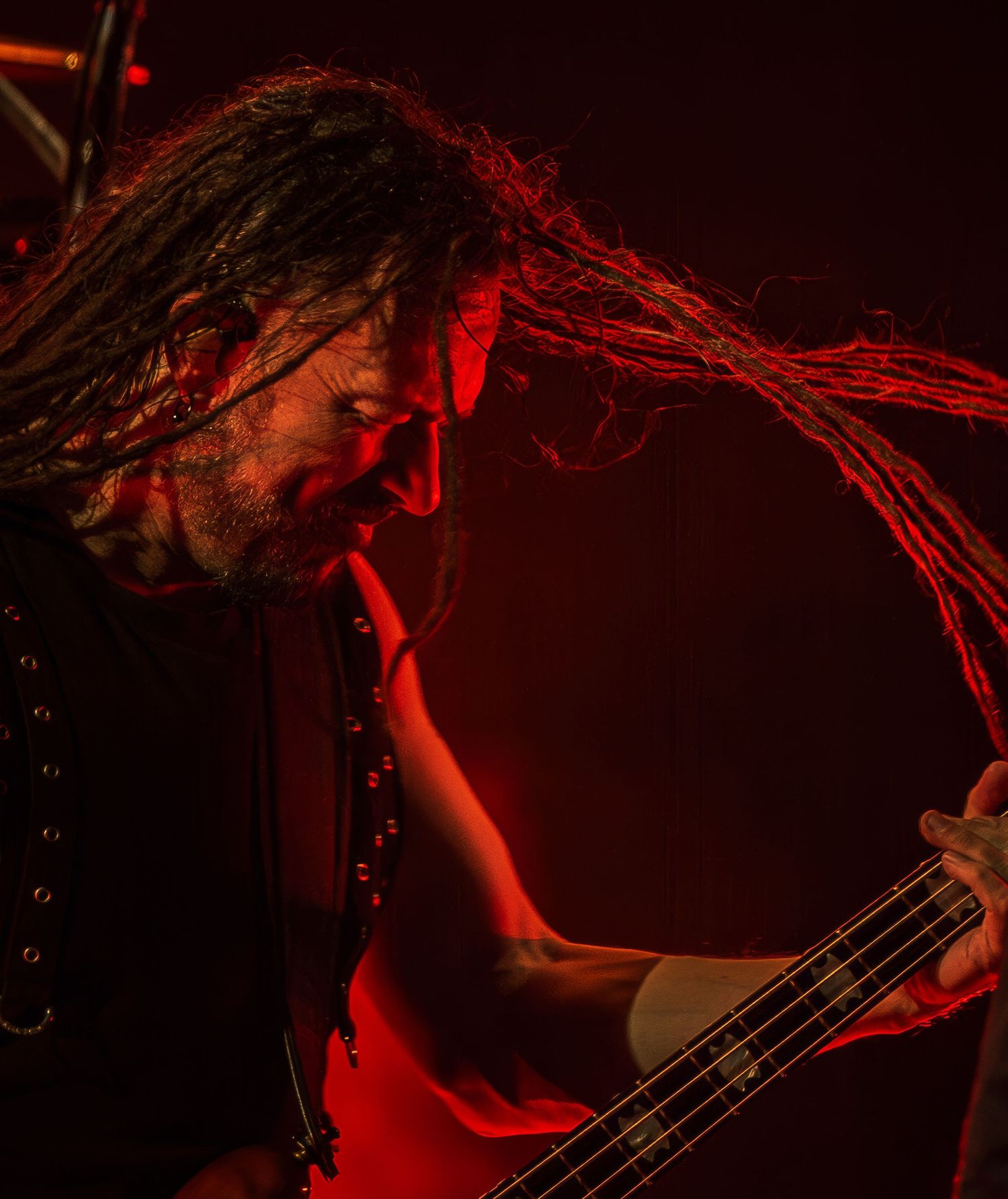 Bass player with long dreadlocks performing under dramatic red stage lighting.