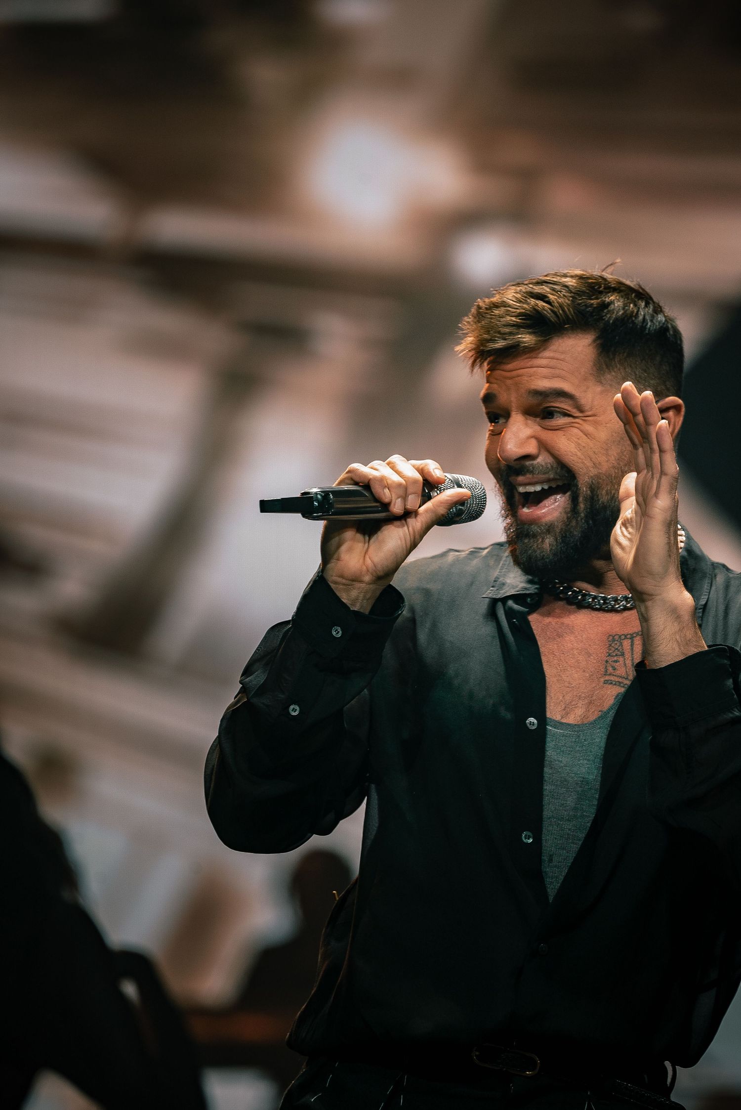 Performer in black jacket singing passionately into handheld microphone.