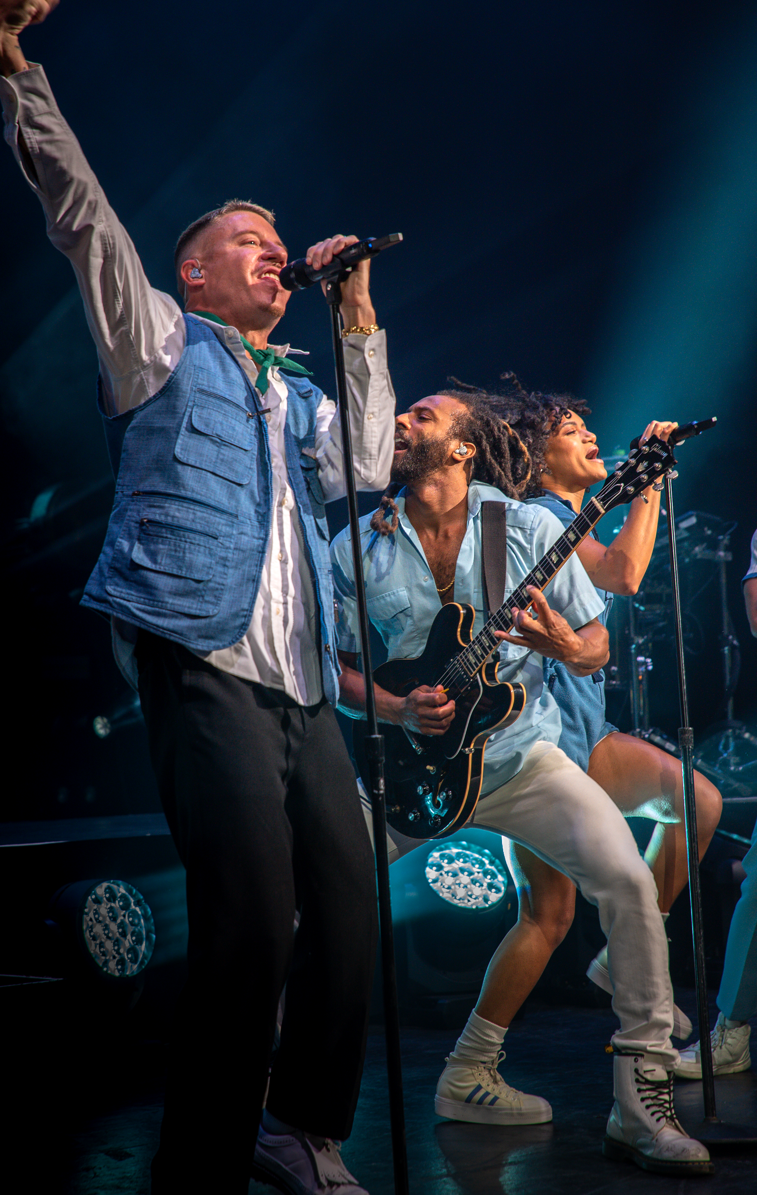 Band members in blue vests performing together on stage with dramatic lighting effects.