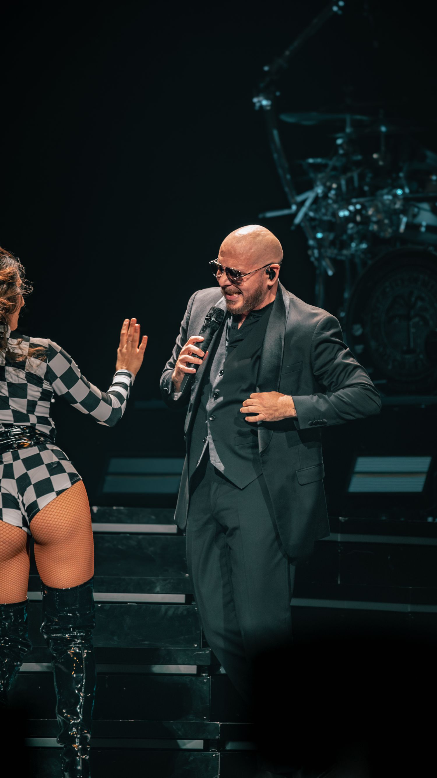 Performers in black suit and checkered outfit interacting during stage performance.