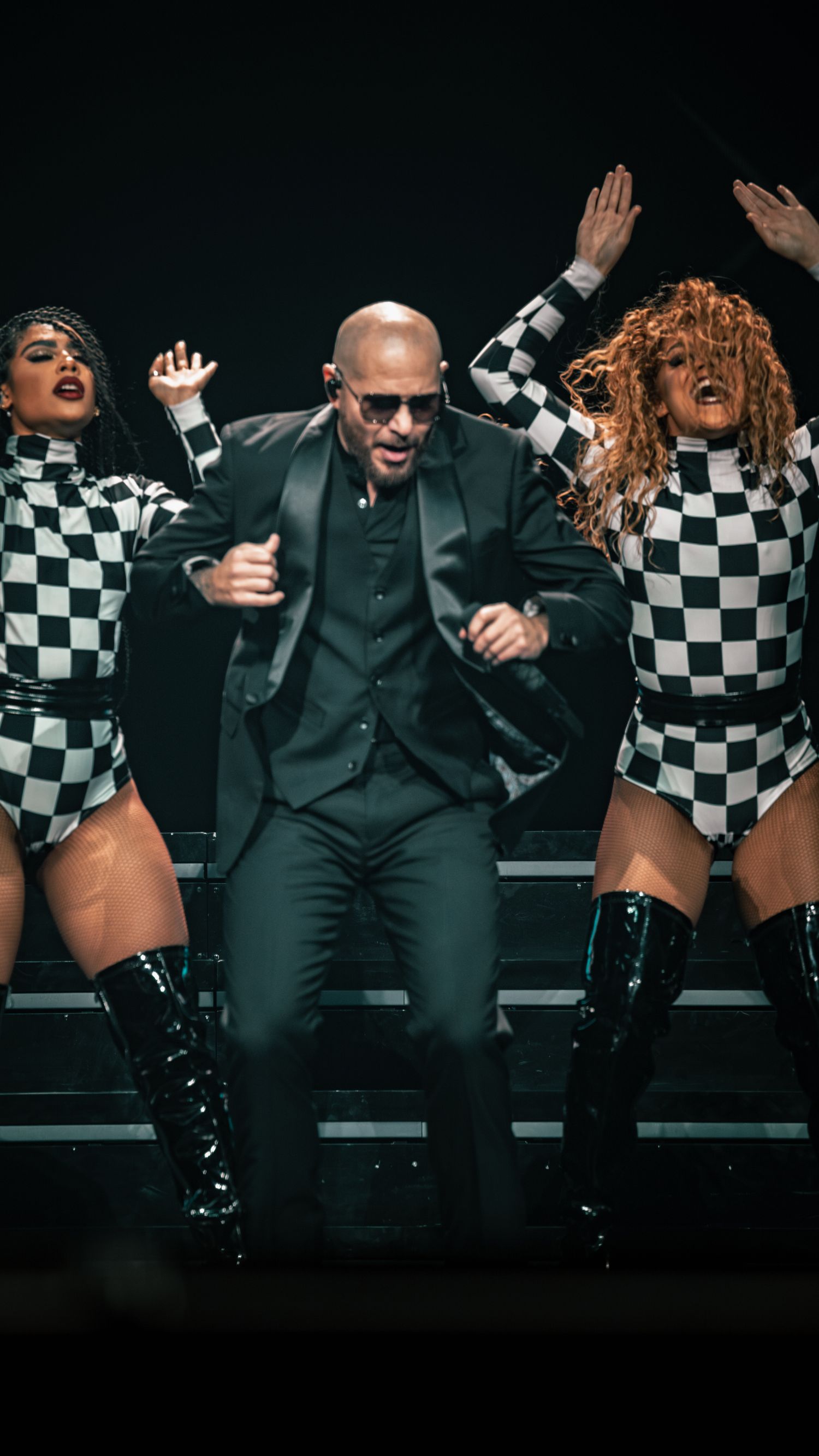 High-energy dance performance with performers in matching checkered outfits on dark stage.