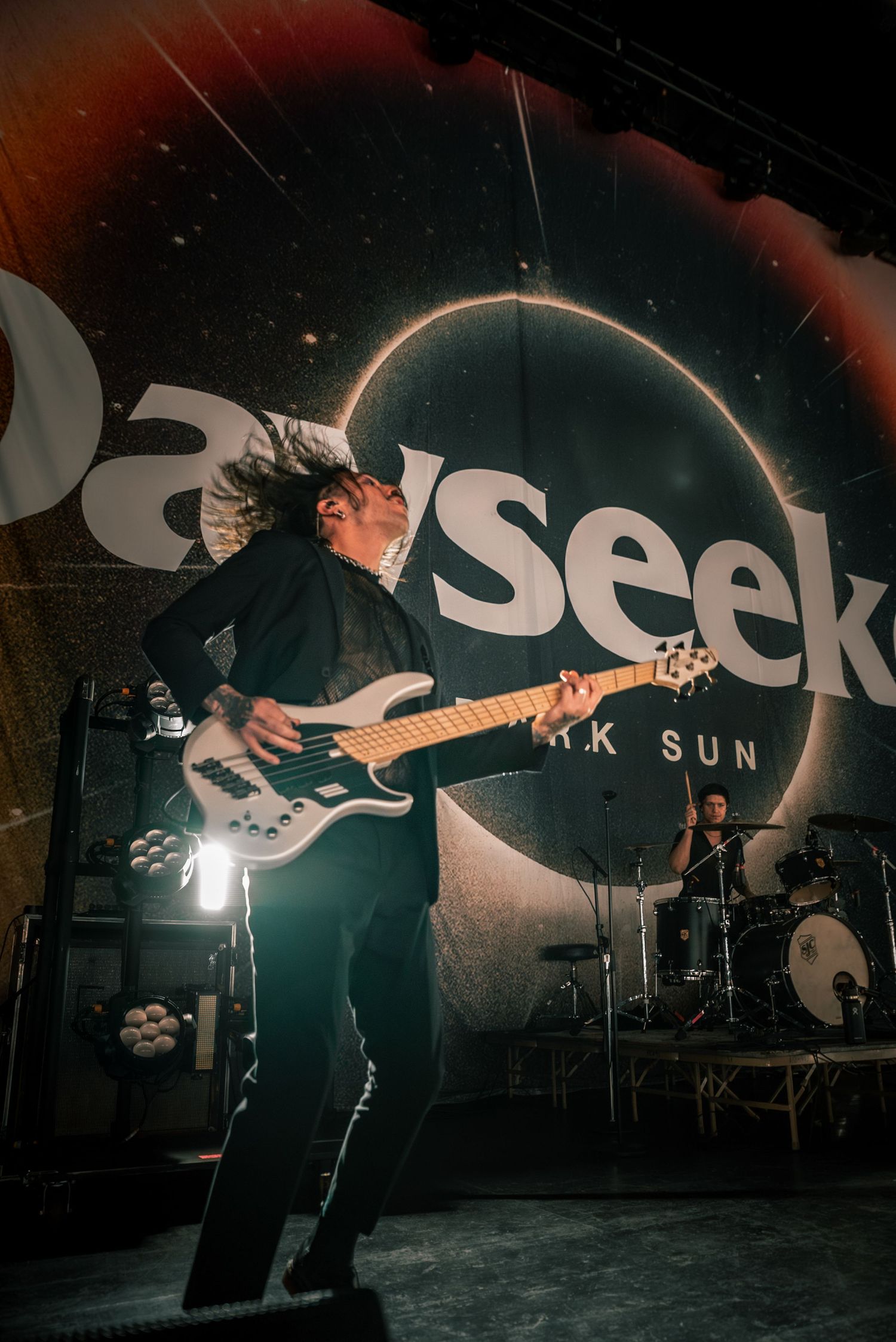 Guitarist performs under band logo with dramatic backlighting on concert stage.