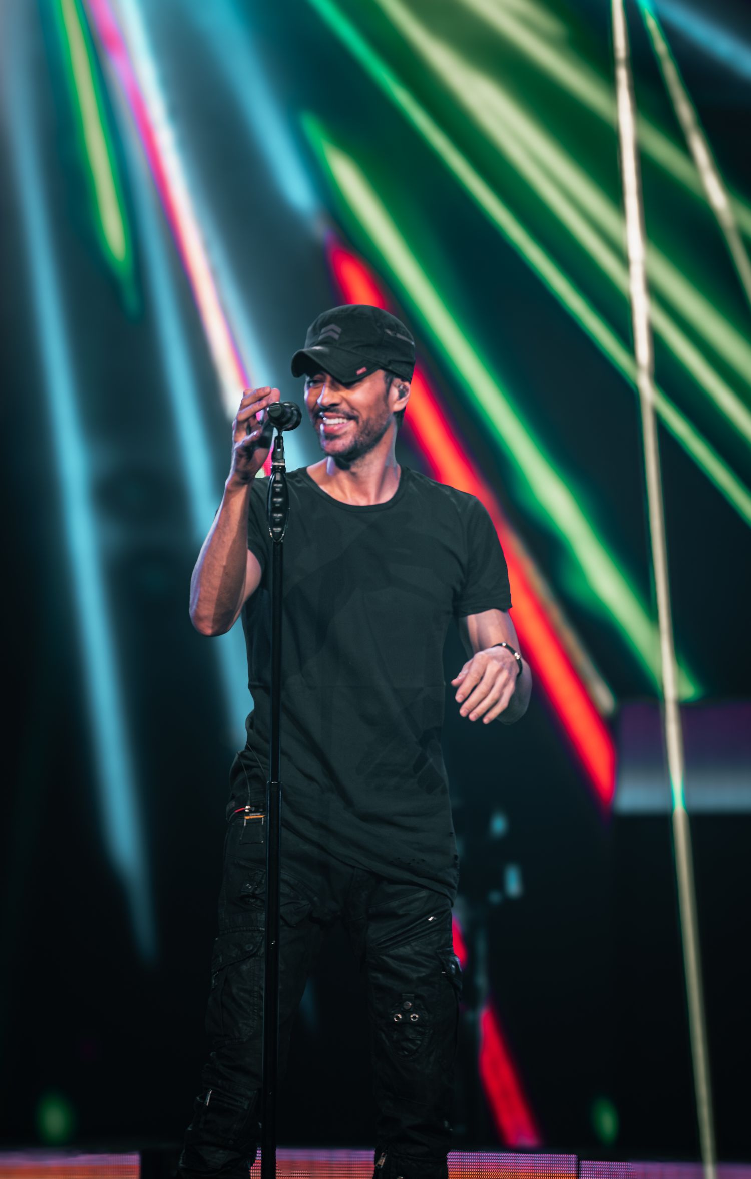 Singer performing on stage with vibrant green and blue lighting effects in background.