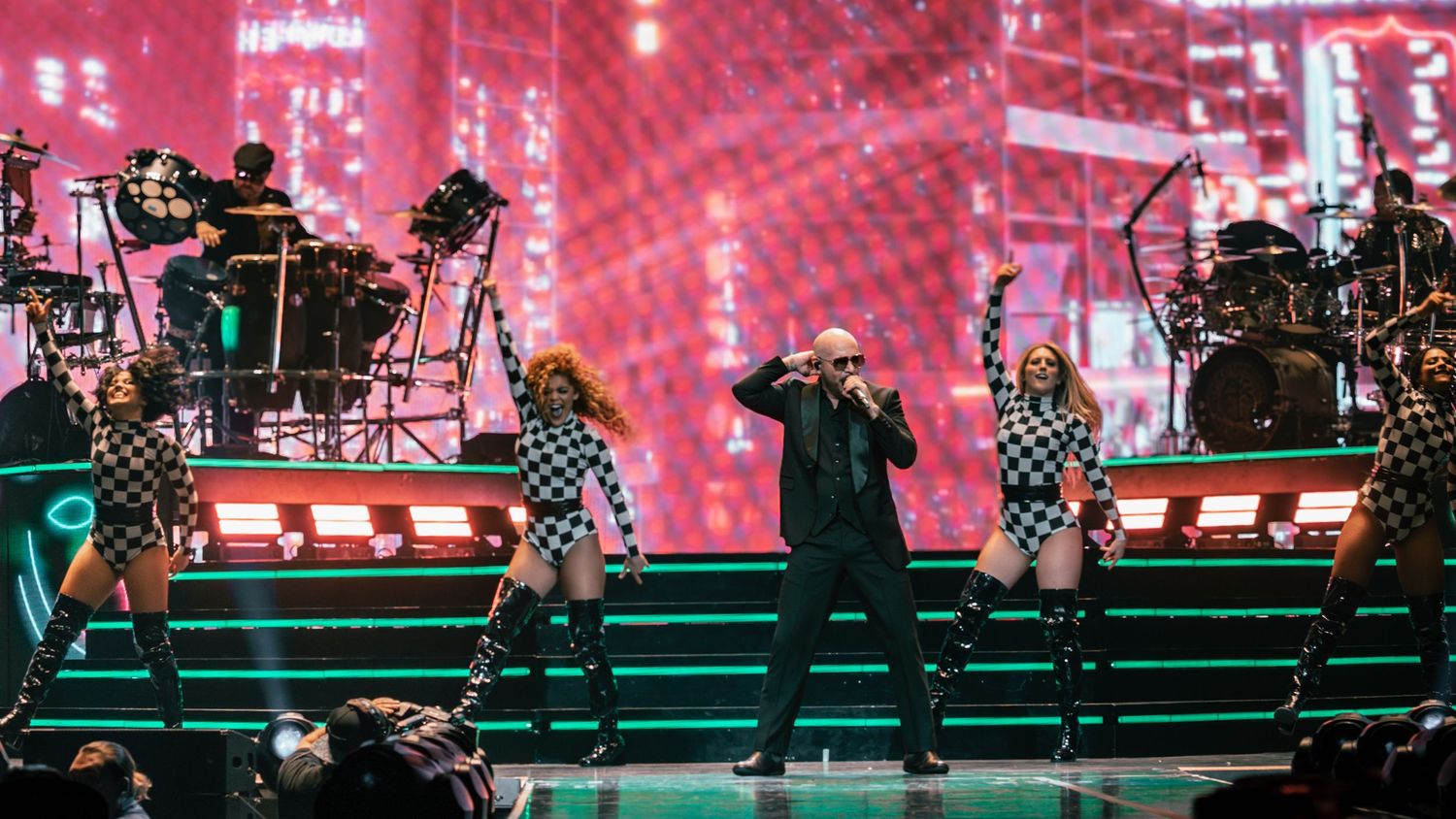 Concert stage performance with dramatic red lighting and illuminated backdrop.