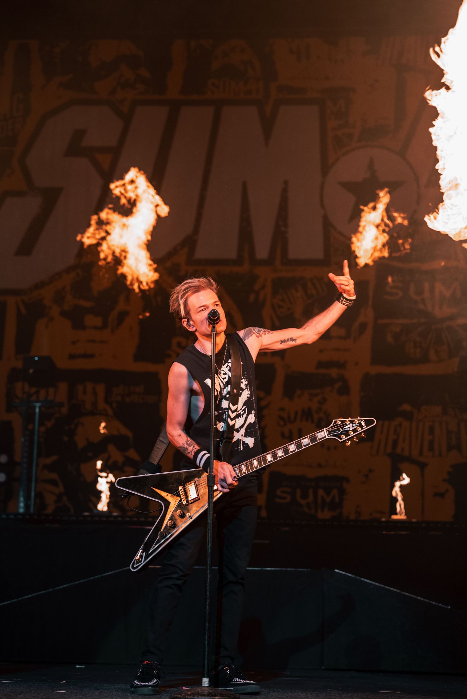 Guitarist performs with fire effects against large text backdrop during rock concert.