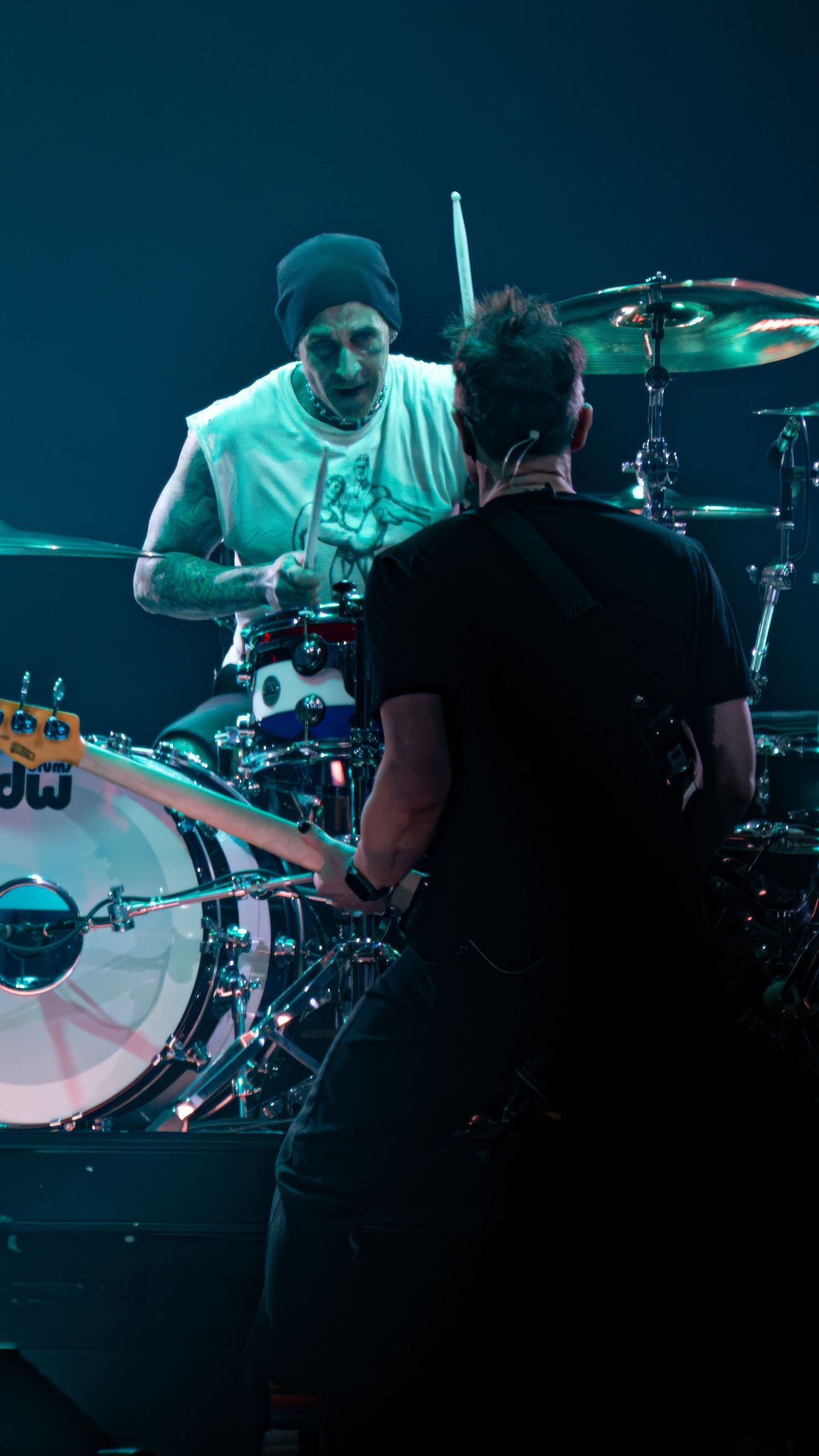 Drummer performs energetically behind drum kit on dimly lit stage during live show.
