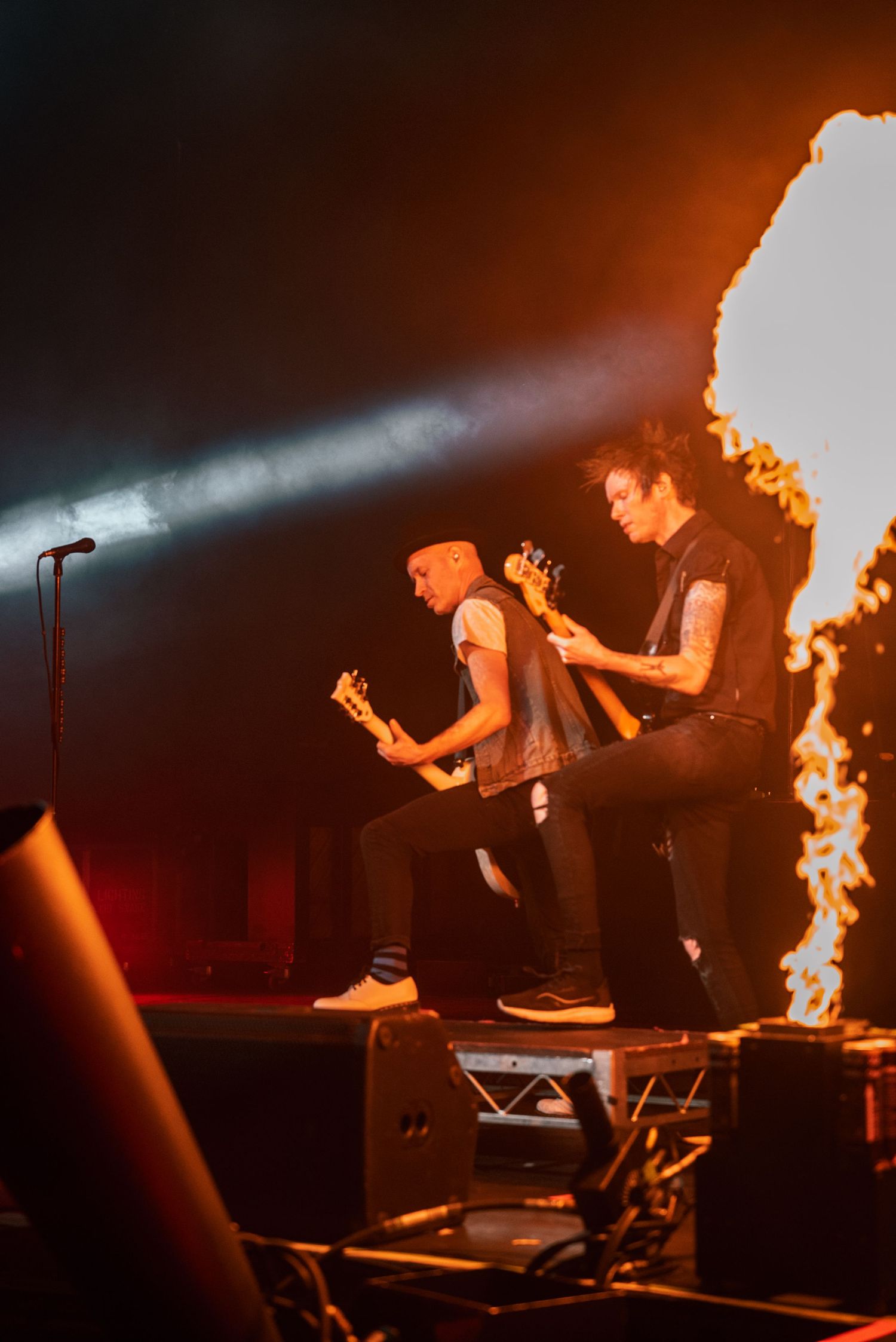 Musicians perform with intense pyrotechnic flames and spotlights on concert stage.