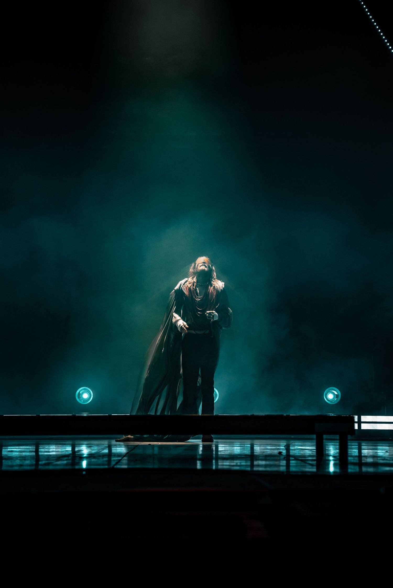 A dramatic concert performance silhouetted against teal lighting on a dark stage.