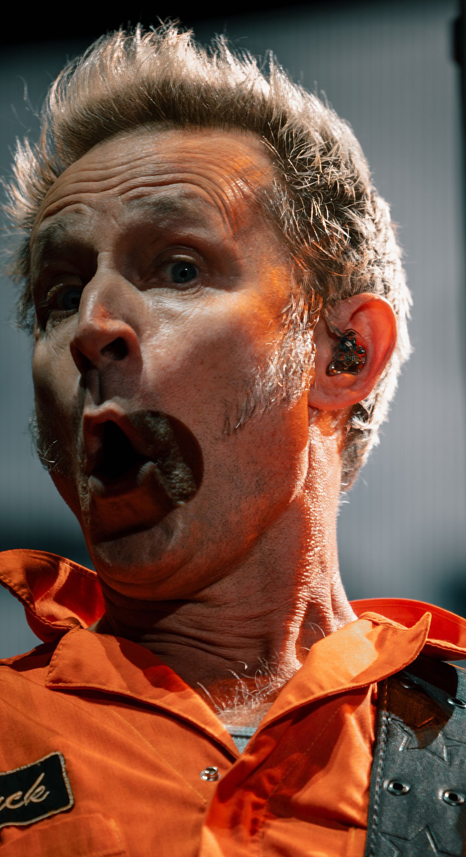 An expressive close-up performance shot with dramatic orange lighting and visible stage sweat.