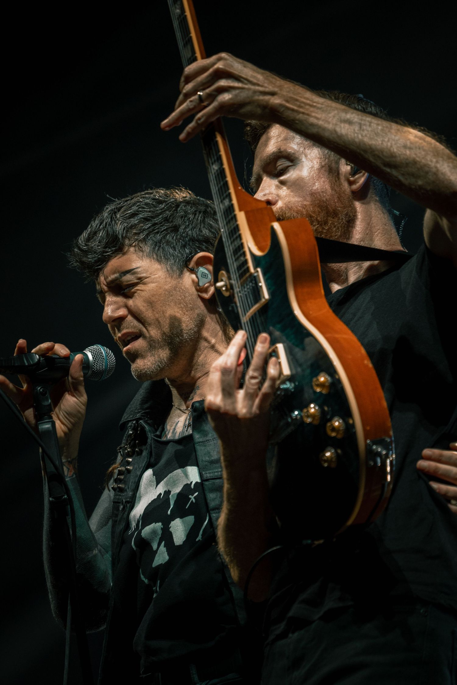 Concert performer singing passionately while playing acoustic guitar in dramatic lighting.
